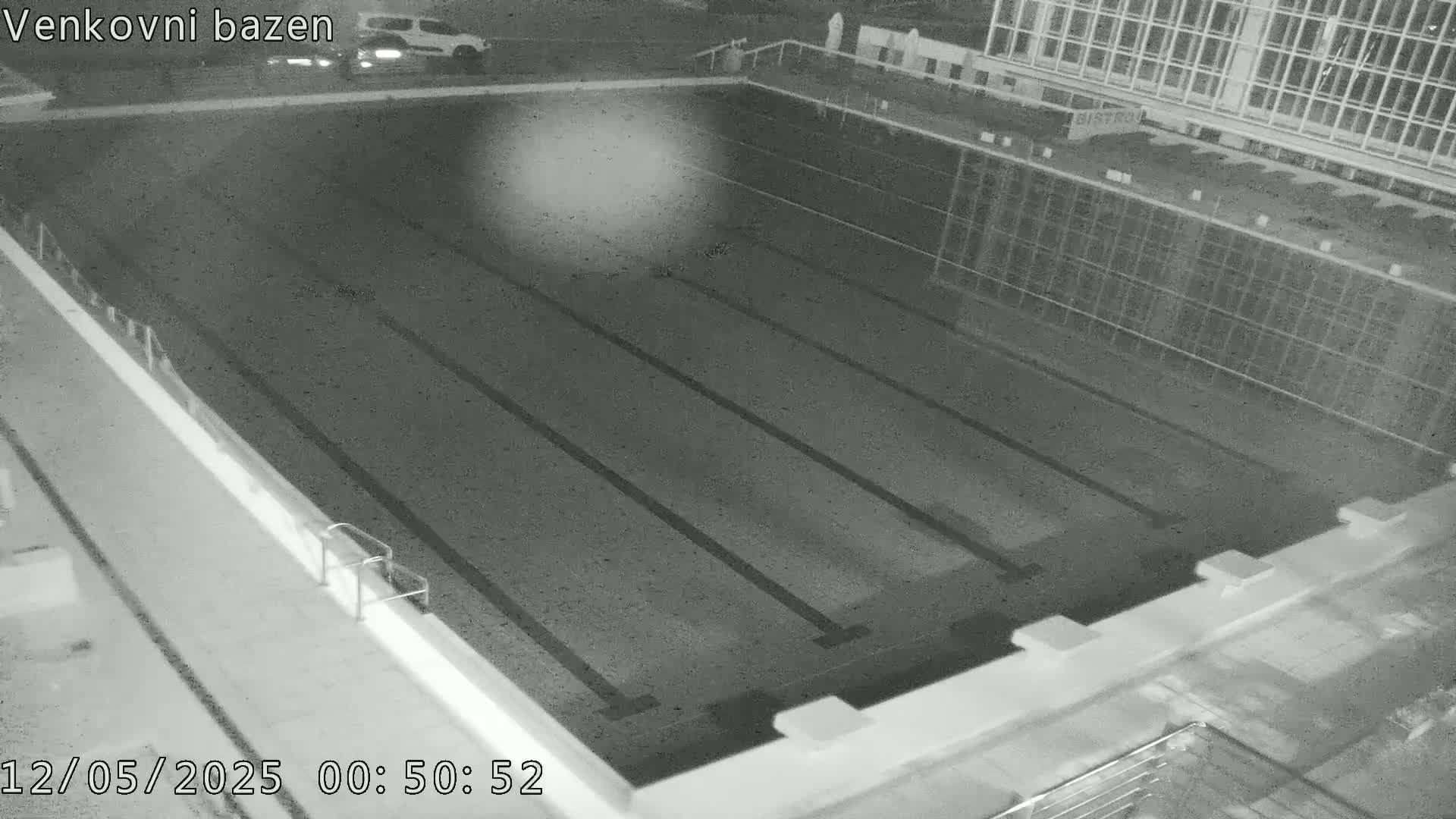 An empty, dark outdoor swimming pool is visible at night.