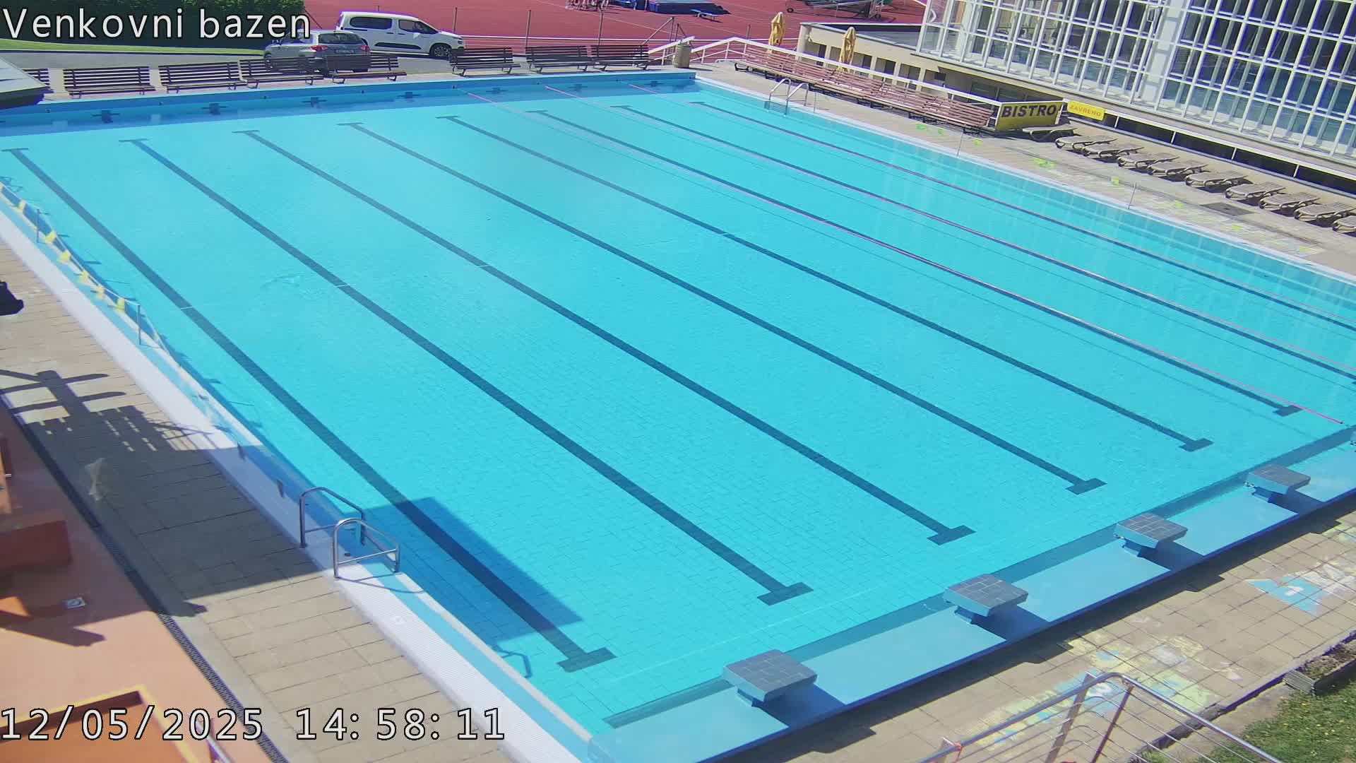 An outdoor swimming pool with multiple lanes is shown on a sunny day.