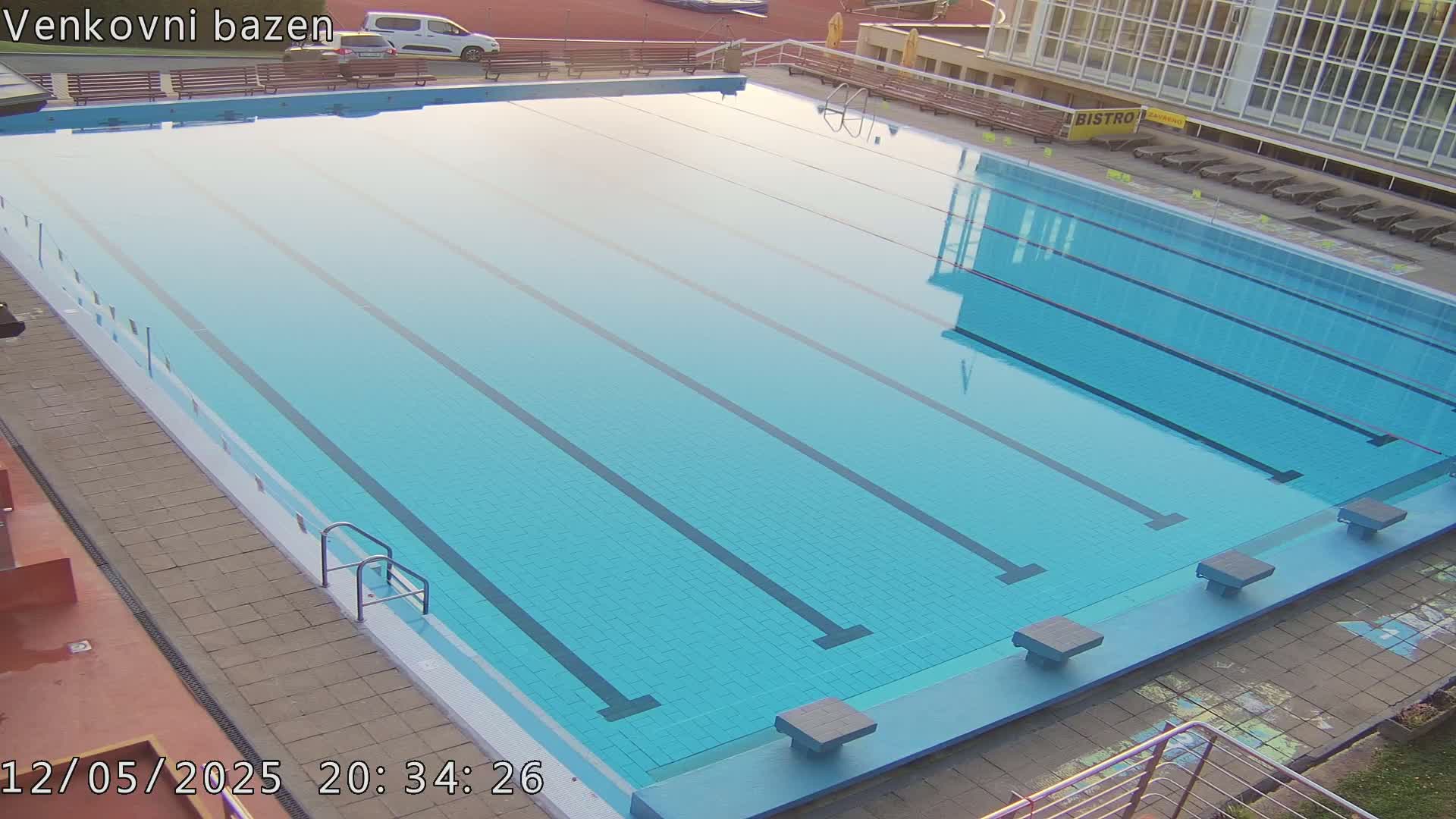 A large, empty outdoor swimming pool with multiple lanes is visible under a calm, clear sky.