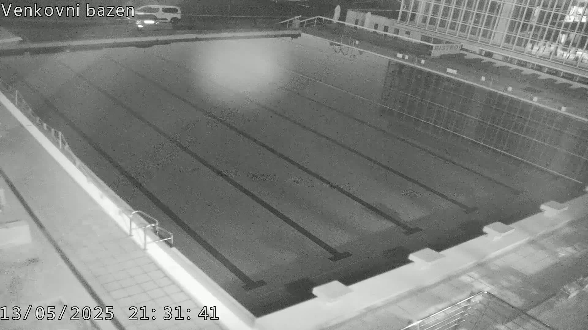 An empty outdoor swimming pool is viewed at night.