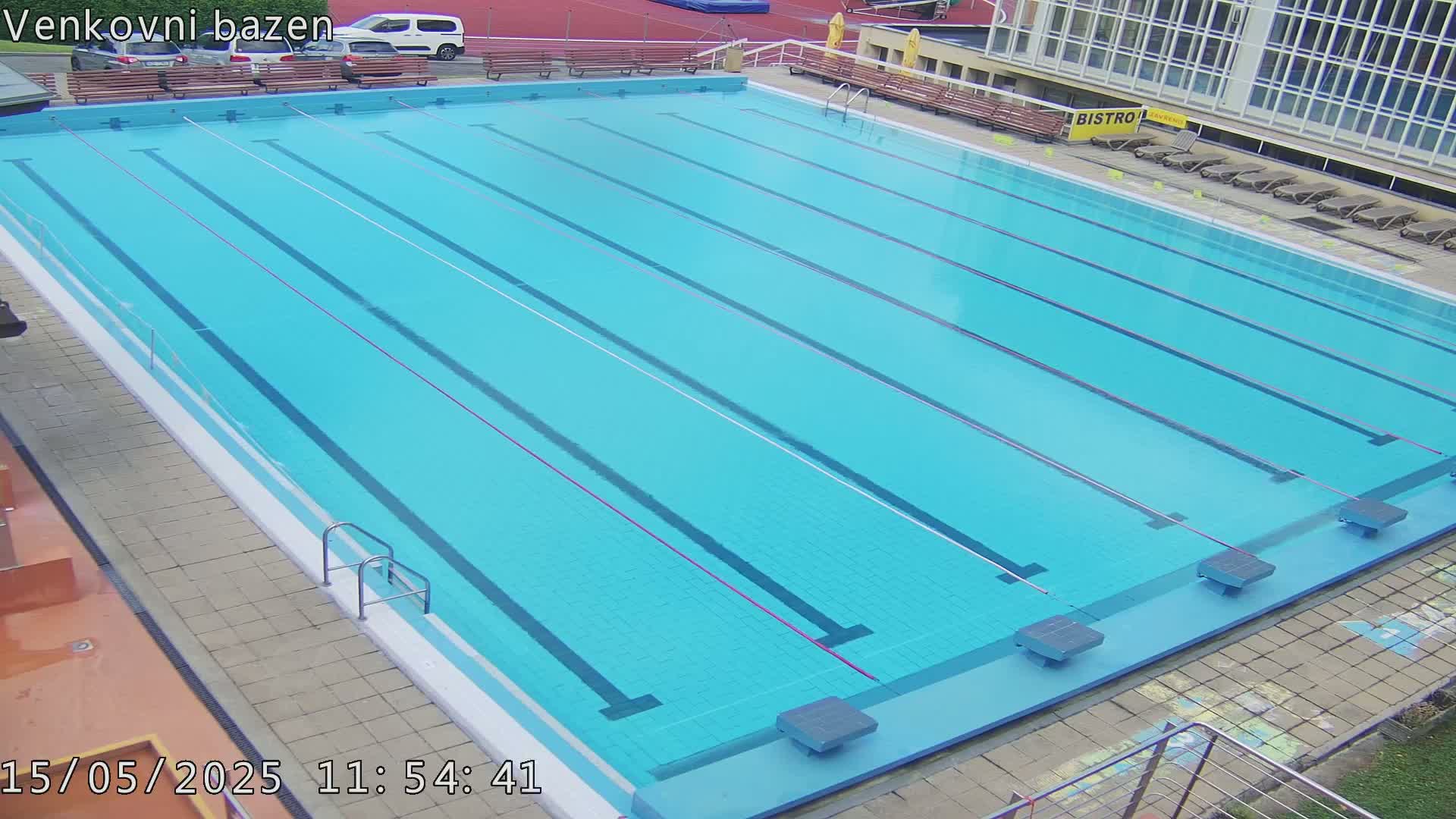 An outdoor swimming pool with multiple lanes is empty, under a clear sky.