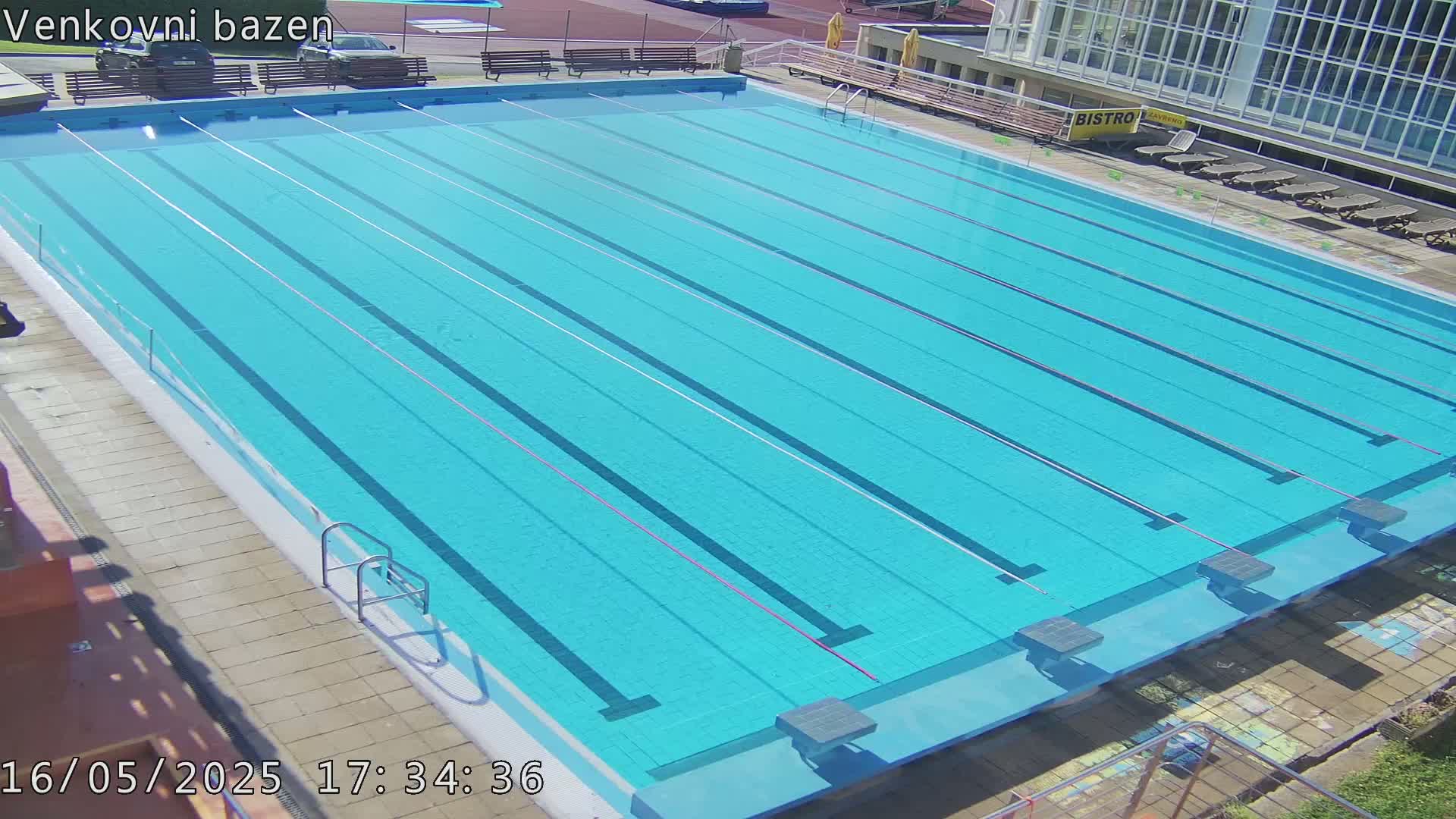 A large, empty outdoor swimming pool with multiple lanes is shown on a sunny day.