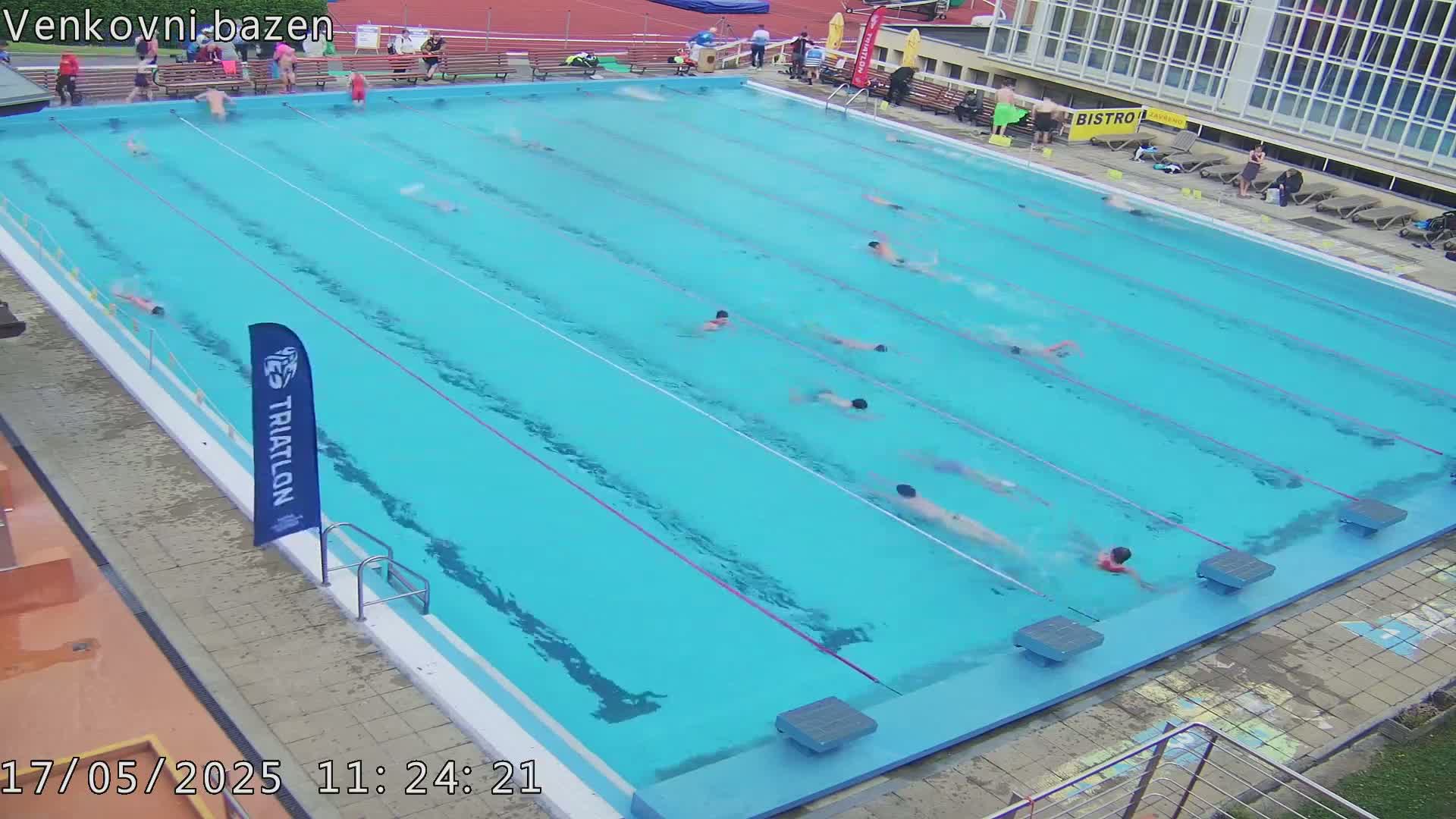 Many people swim laps in a large outdoor pool on a partly cloudy day.