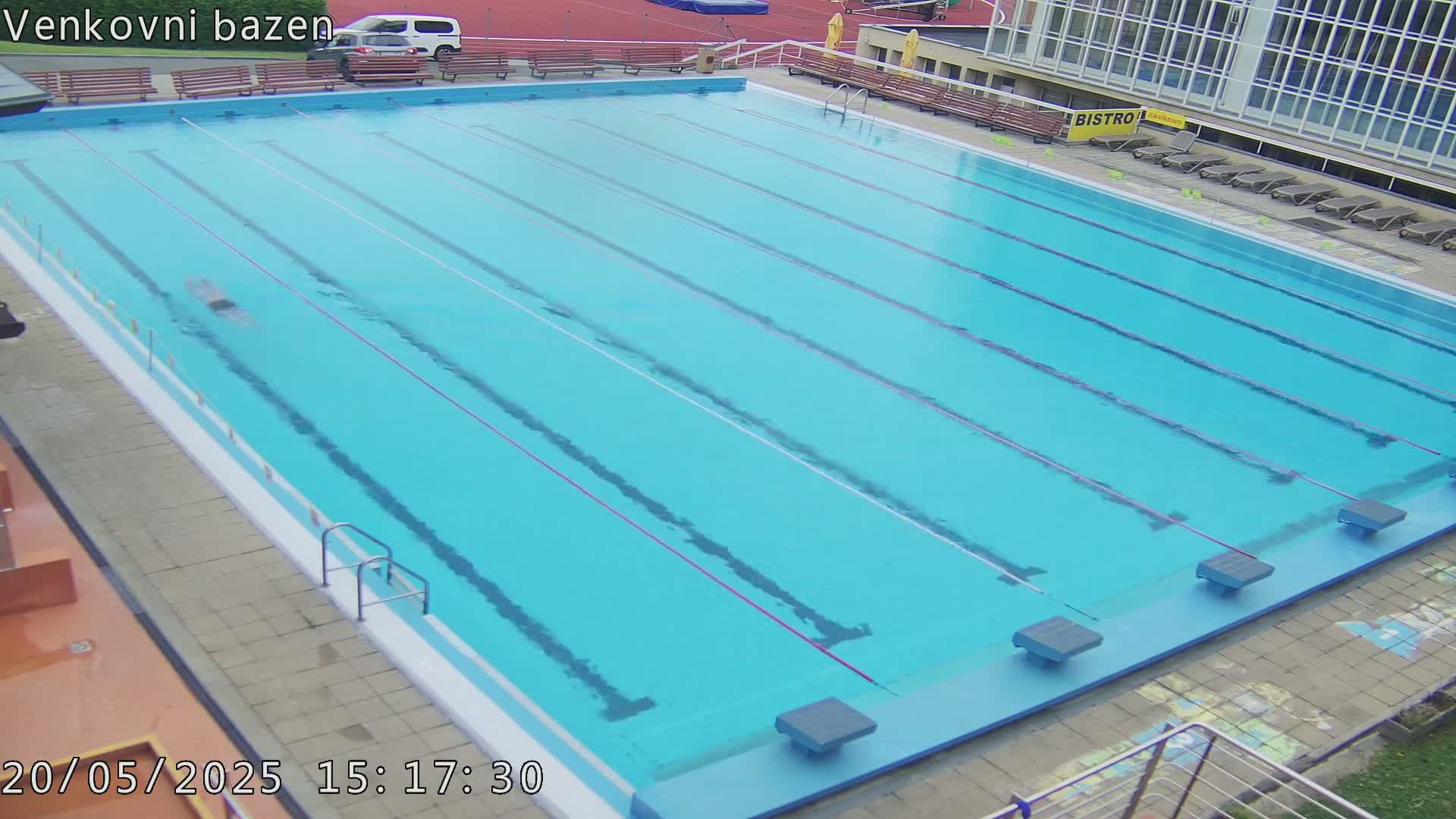 A person swims laps in a light blue outdoor swimming pool on a partly cloudy day.