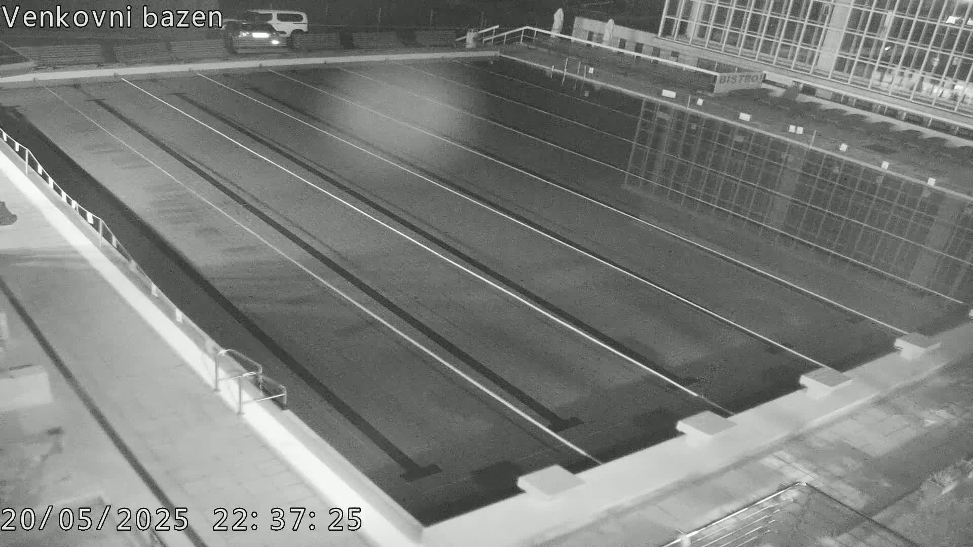 An empty outdoor swimming pool at night is shown, with lane dividers visible in the water.