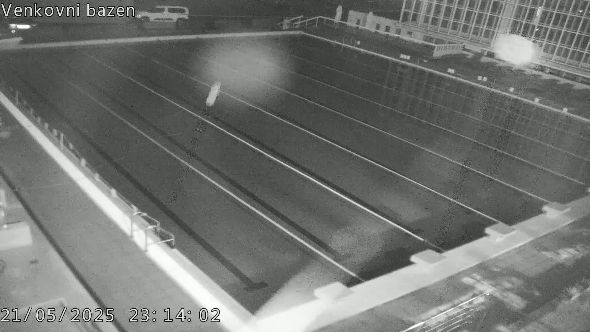 An empty outdoor swimming pool is viewed from above at night.