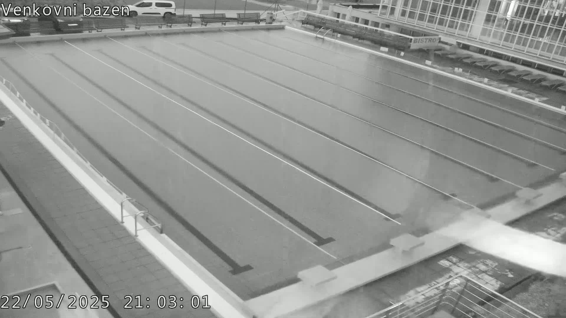 An empty outdoor swimming pool with lane dividers is seen at night under light rain.