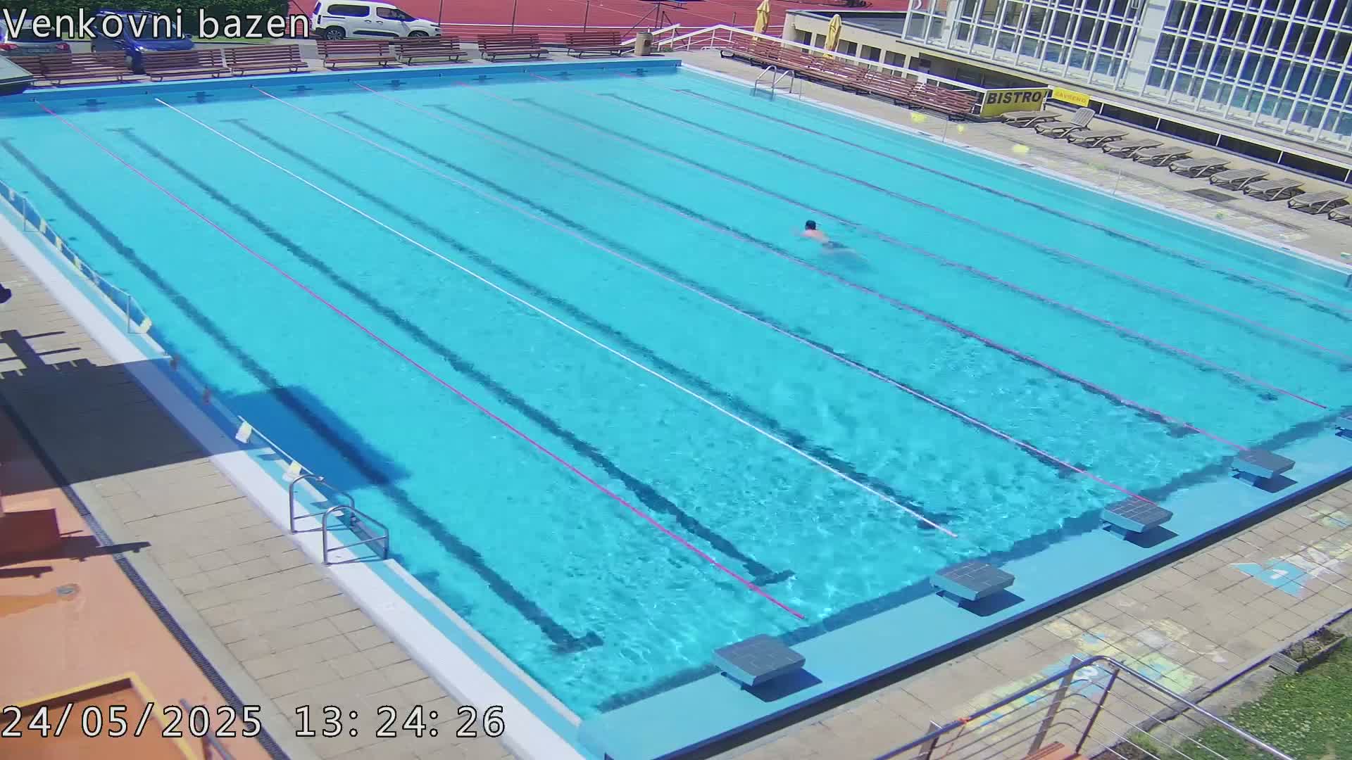 A person swims laps in a sunny outdoor swimming pool with multiple lanes.