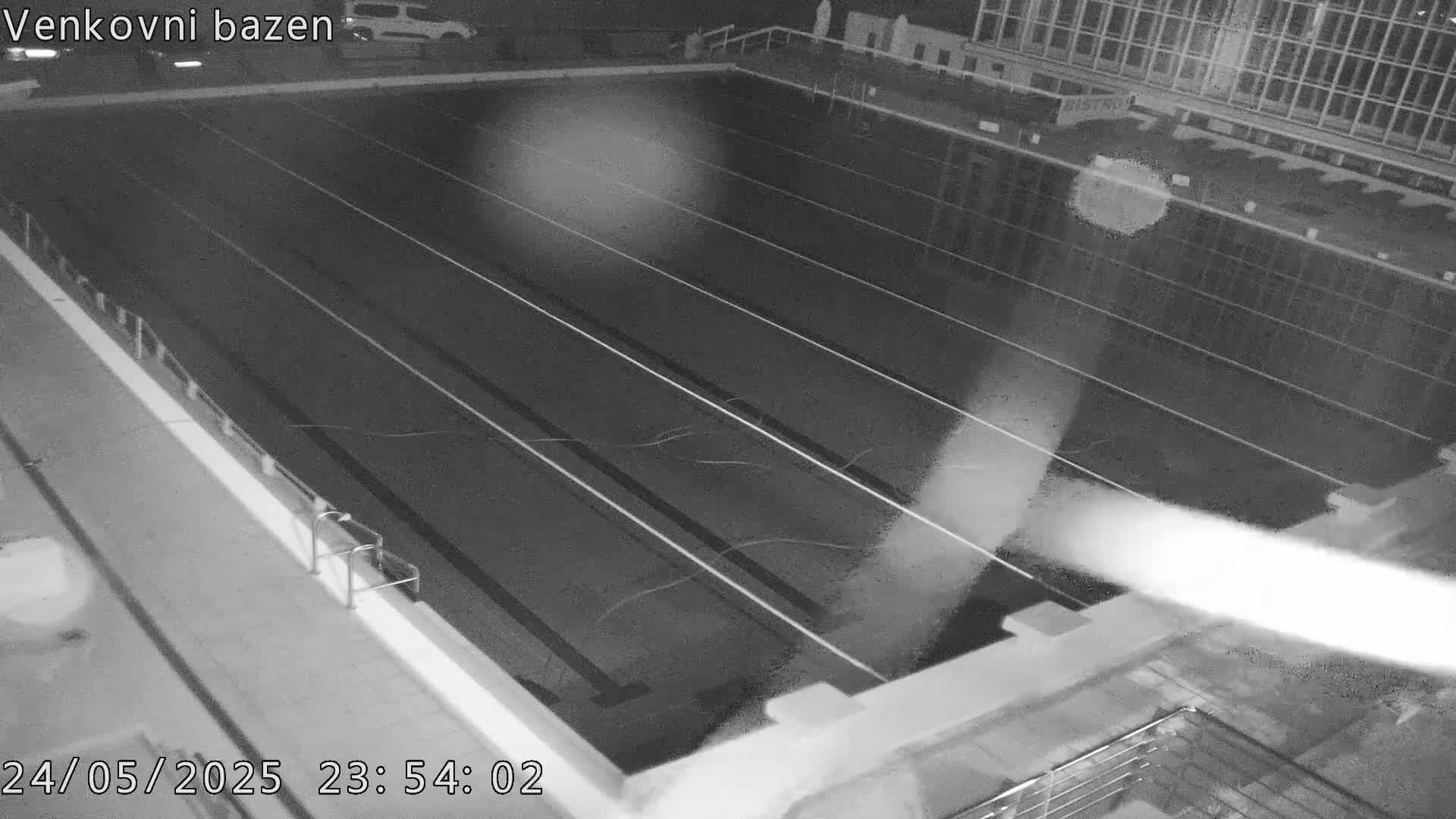 A nighttime, high-angle view shows an empty outdoor swimming pool with lane dividers.