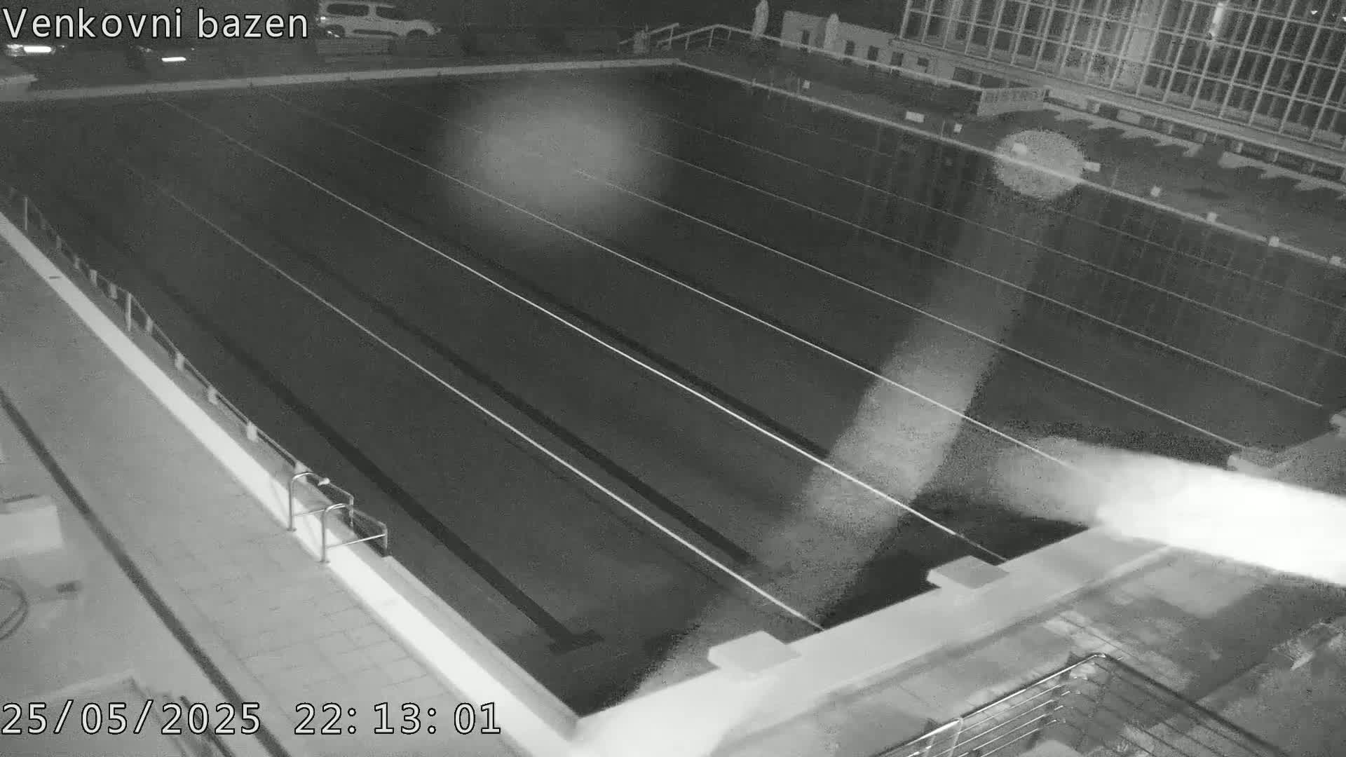 An empty, dark outdoor swimming pool is seen at night.