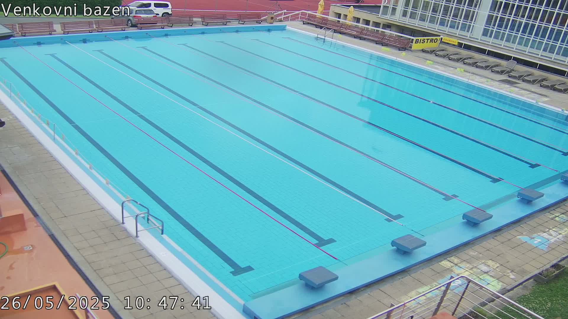 An outdoor swimming pool with multiple lanes is mostly empty under a clear sky.