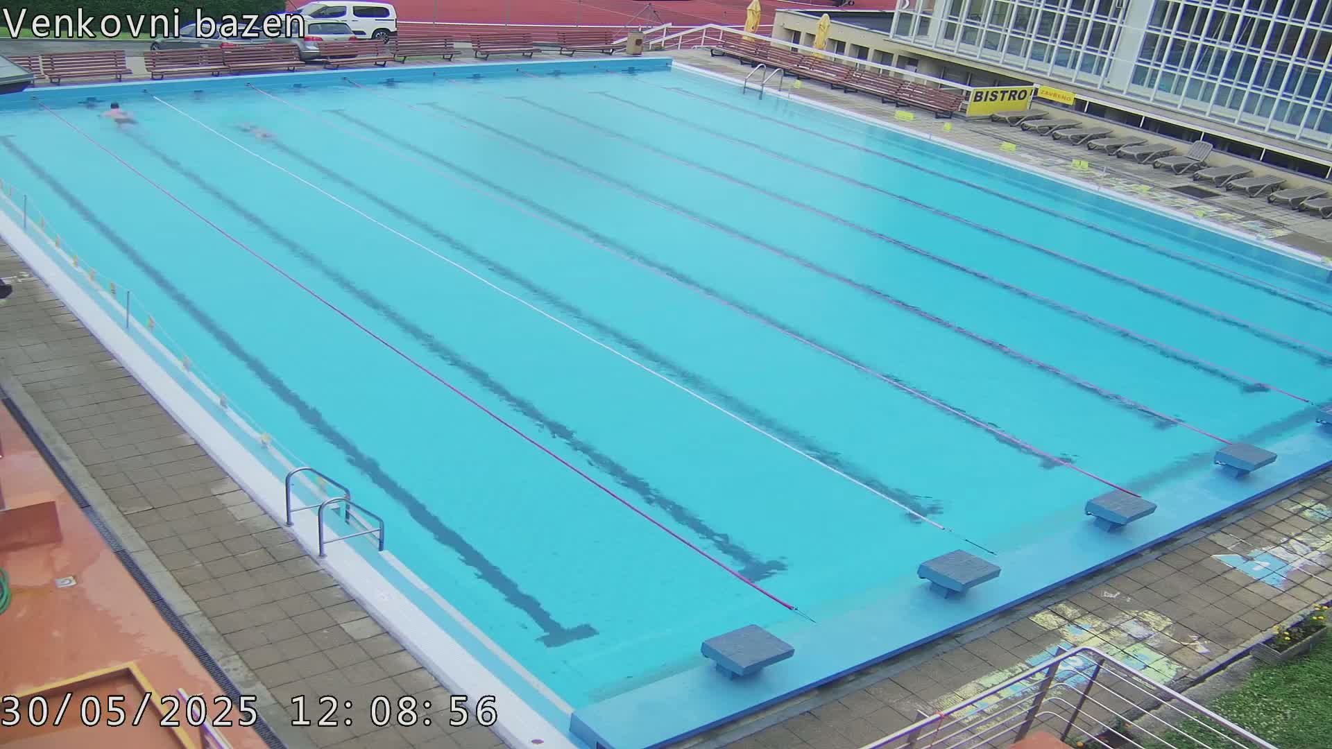 An outdoor swimming pool with several lanes and a few people swimming in it.