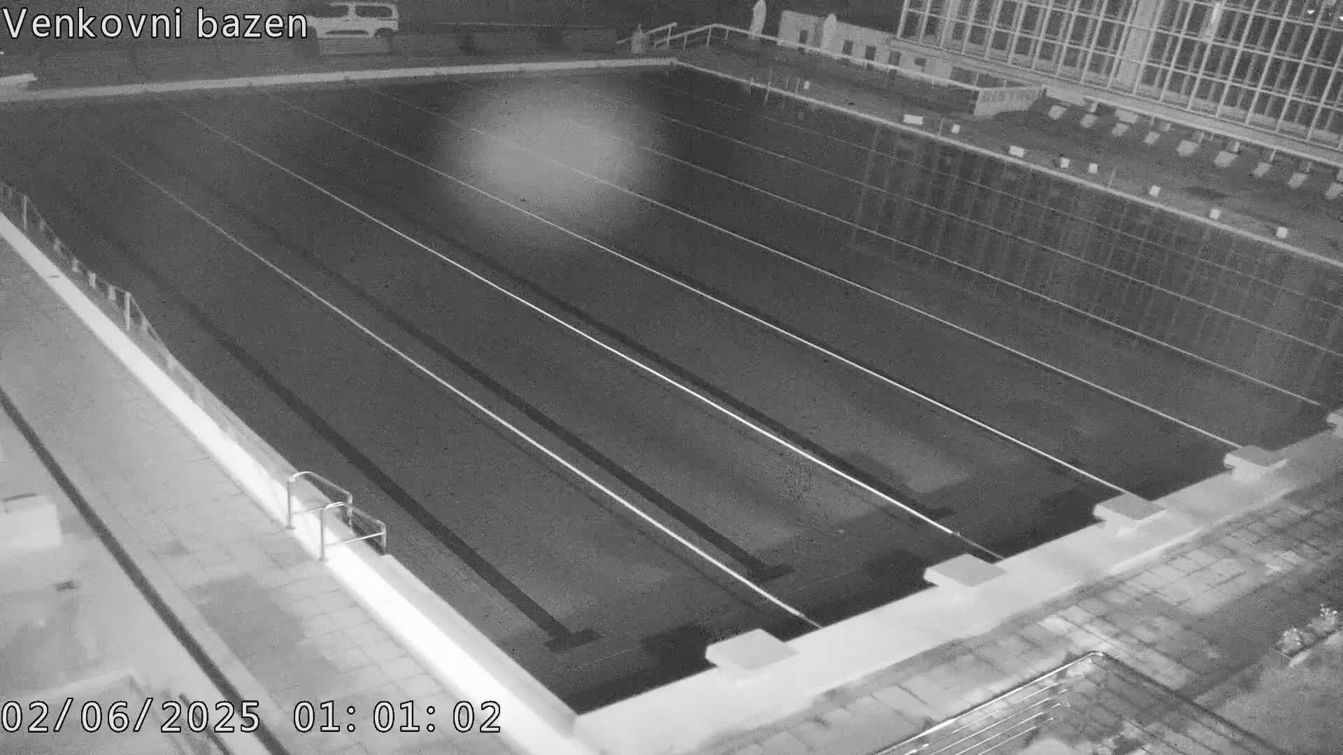 An empty, dark swimming pool with several lanes is seen at night.