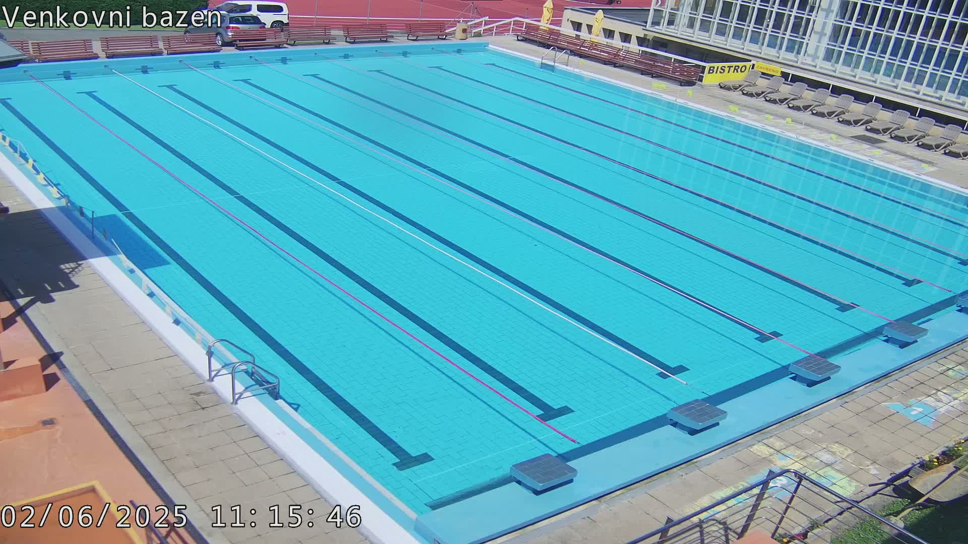 An outdoor swimming pool with multiple lanes is shown on a sunny day.