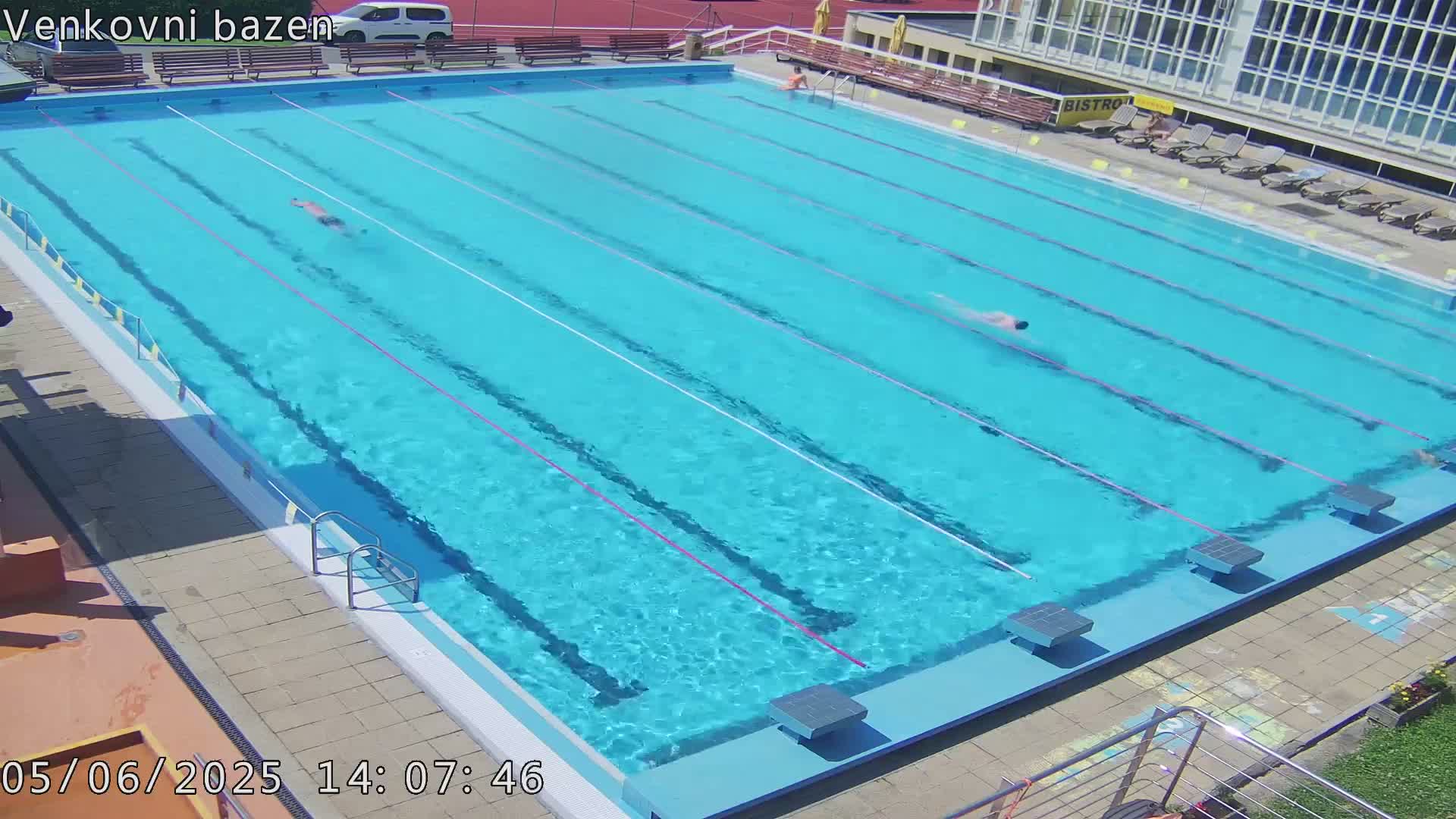 An outdoor swimming pool with two people swimming laps in the bright sunlight.