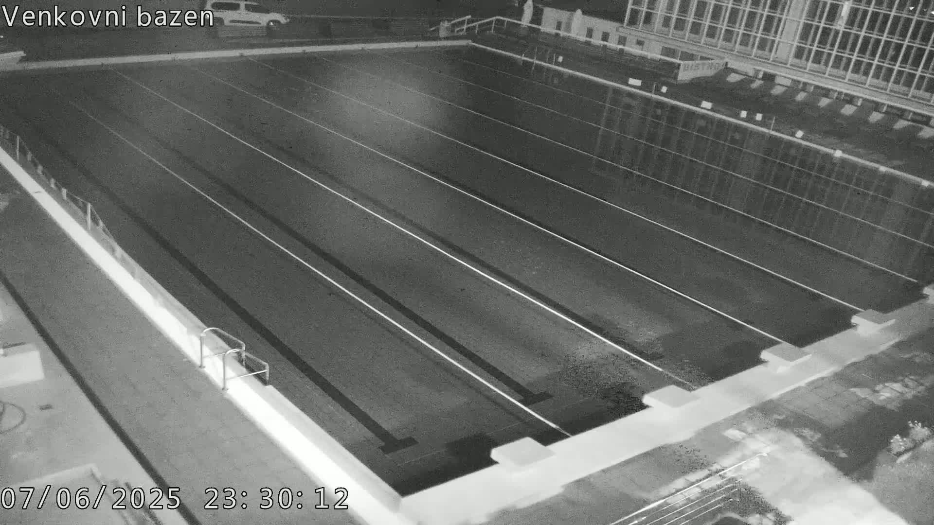 An empty outdoor swimming pool at night is seen from above, showing multiple lanes.