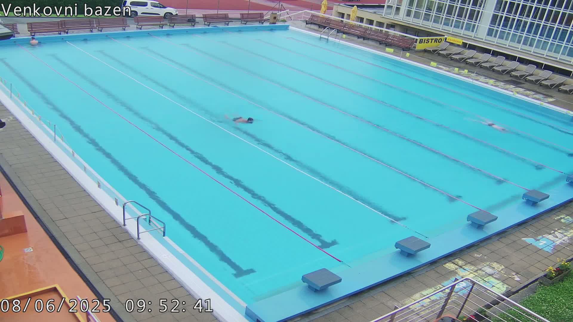 An outdoor swimming pool with several lanes and a few people swimming in it.