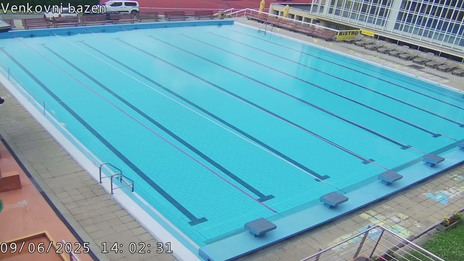 An outdoor swimming pool with multiple lanes is mostly empty, under a clear sky.