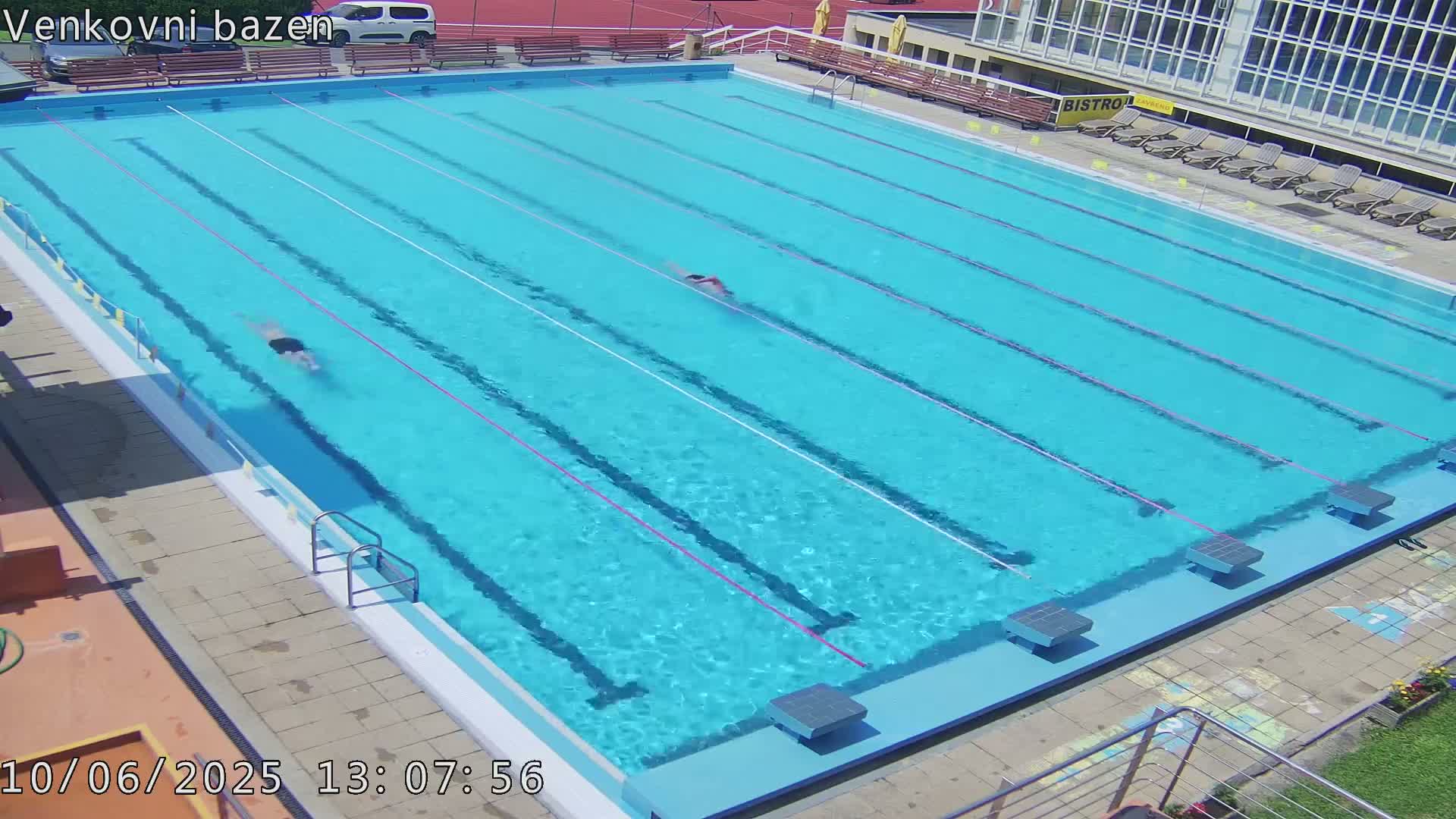 An outdoor swimming pool with two people swimming laps on a sunny day.