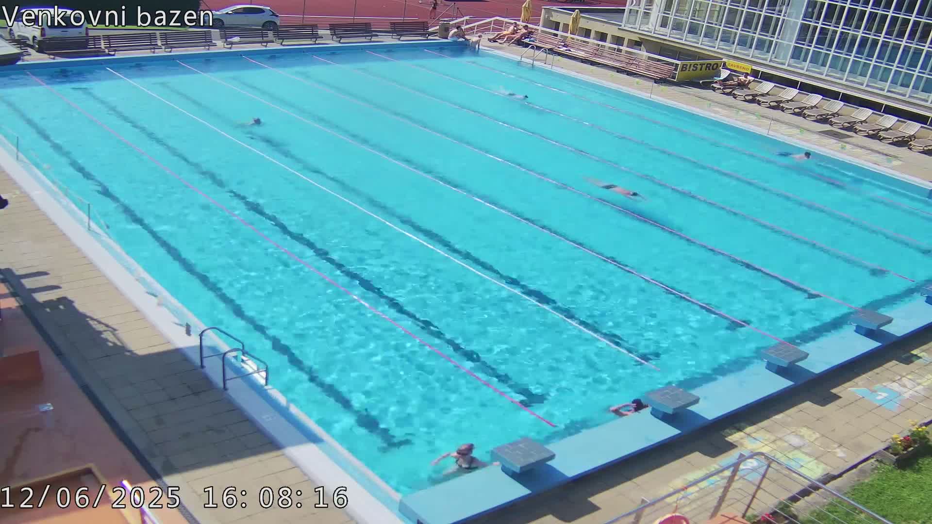 A large outdoor swimming pool with several people swimming in it on a sunny day.
