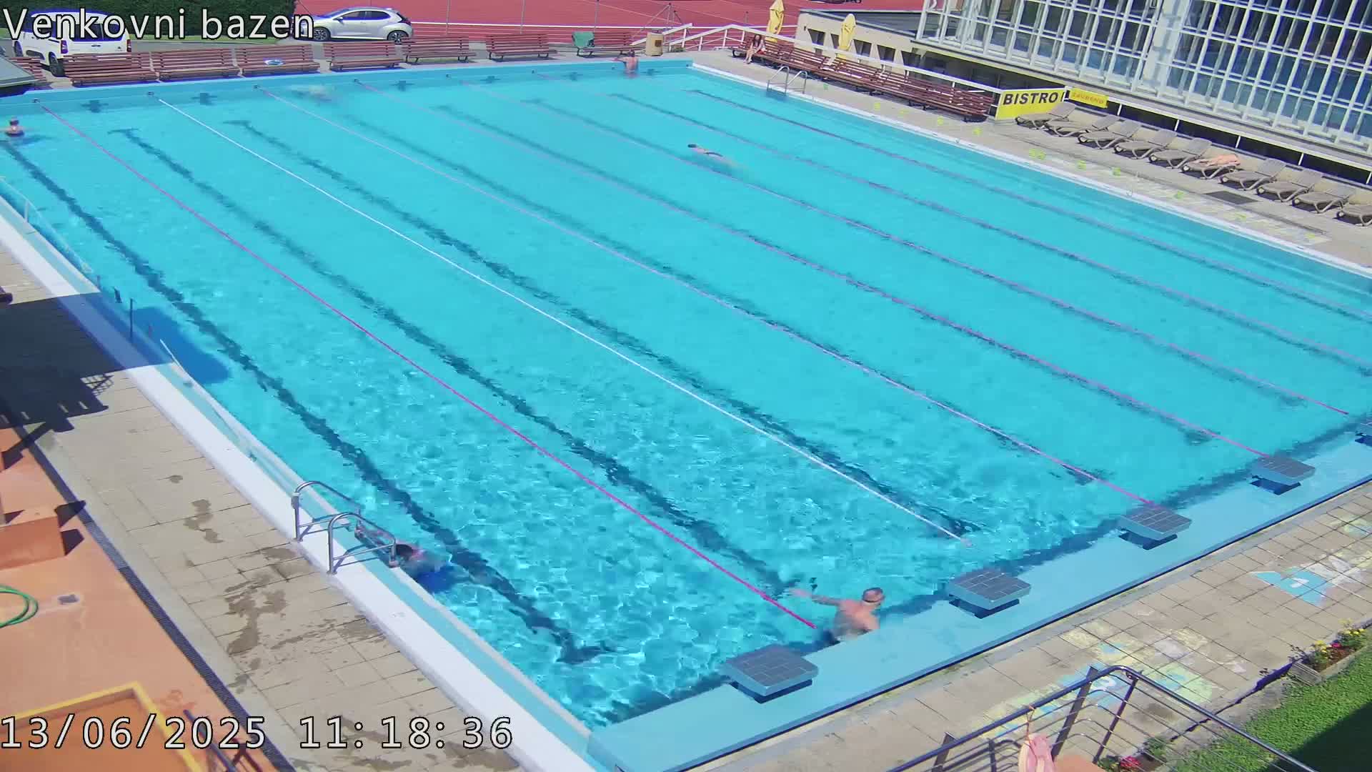 An outdoor swimming pool with several people swimming in it on a sunny day.