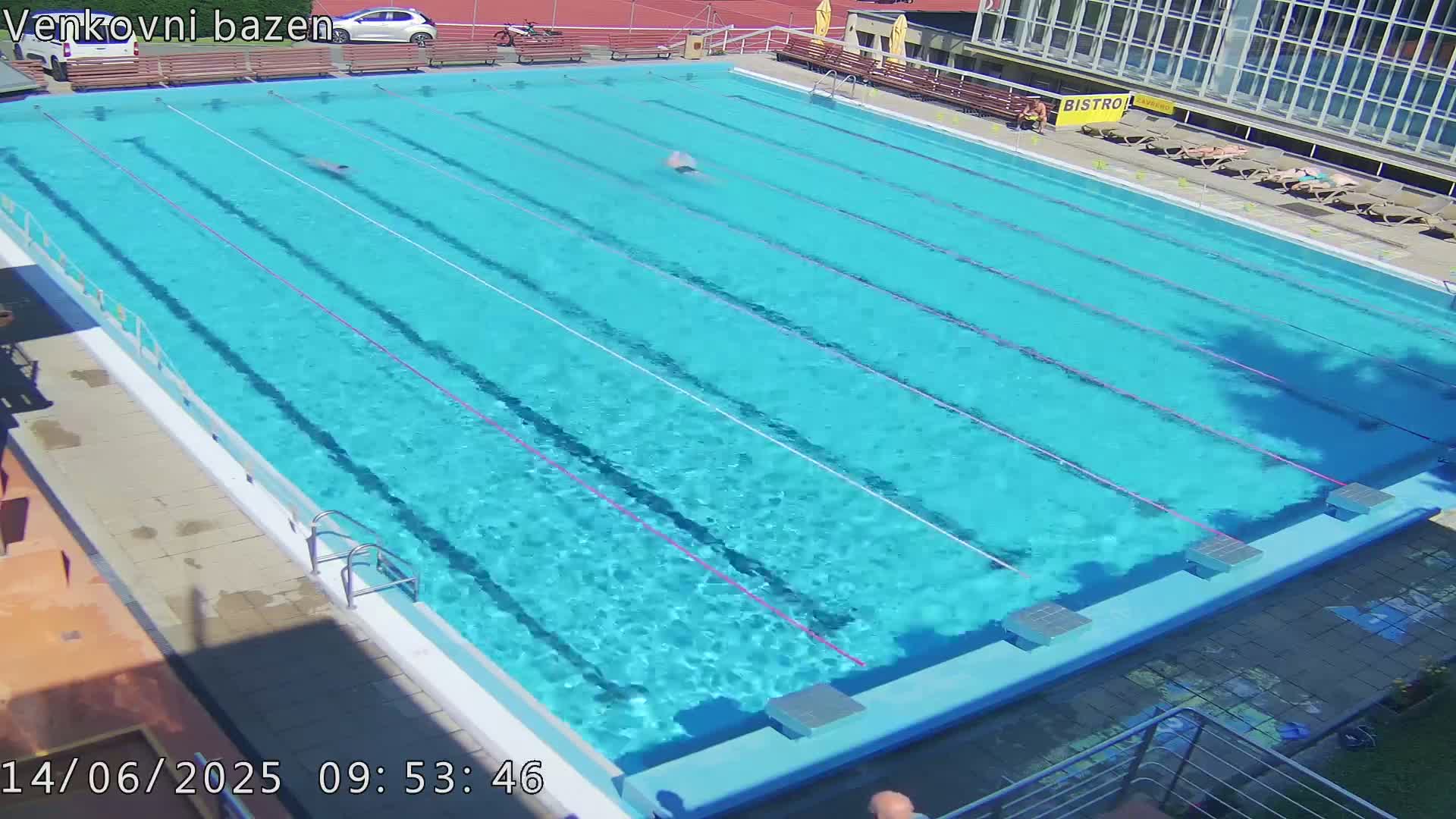 A large outdoor swimming pool with two people swimming laps on a sunny day.