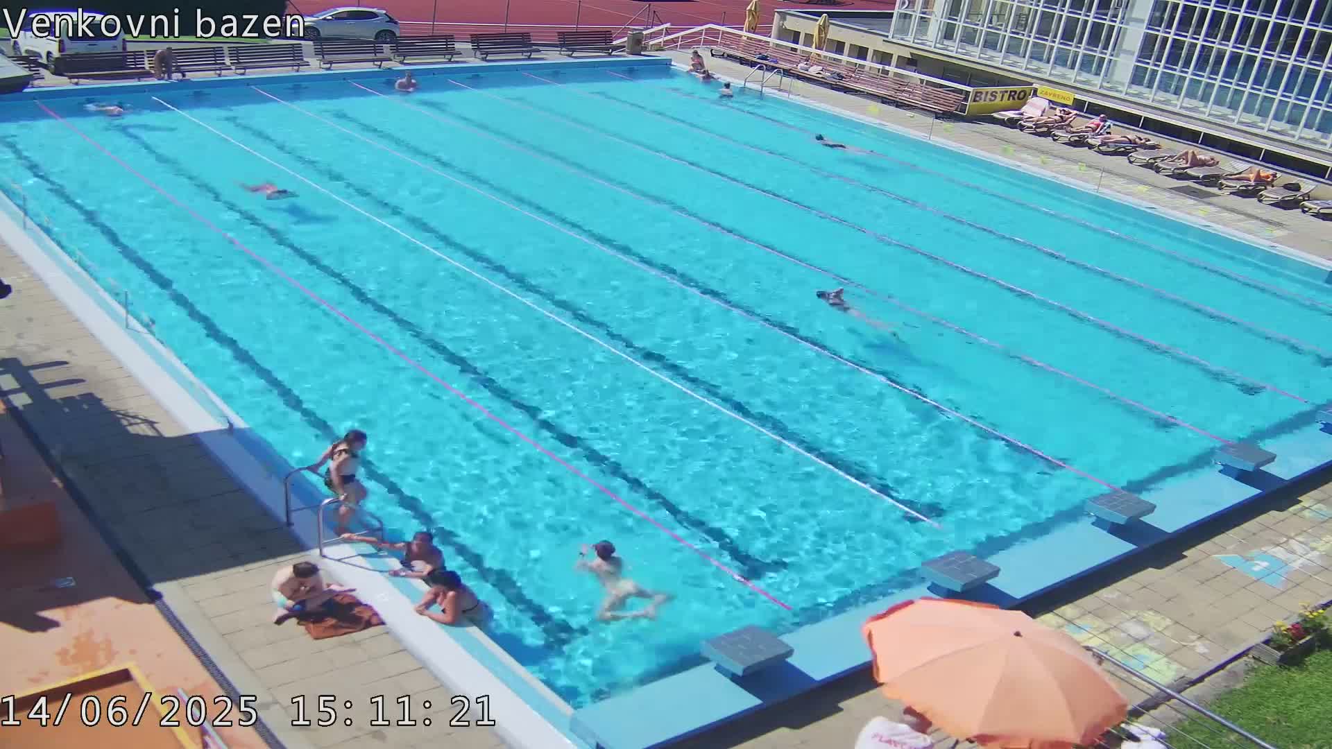 A sunny outdoor swimming pool with several people swimming and lounging around the edge.