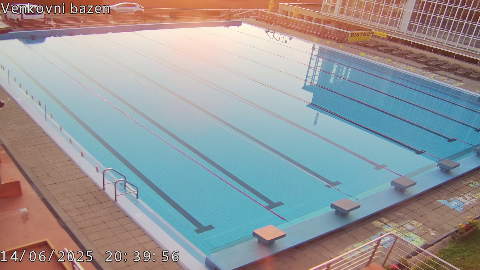 A sunny outdoor swimming pool with several people swimming and lounging around the edge.