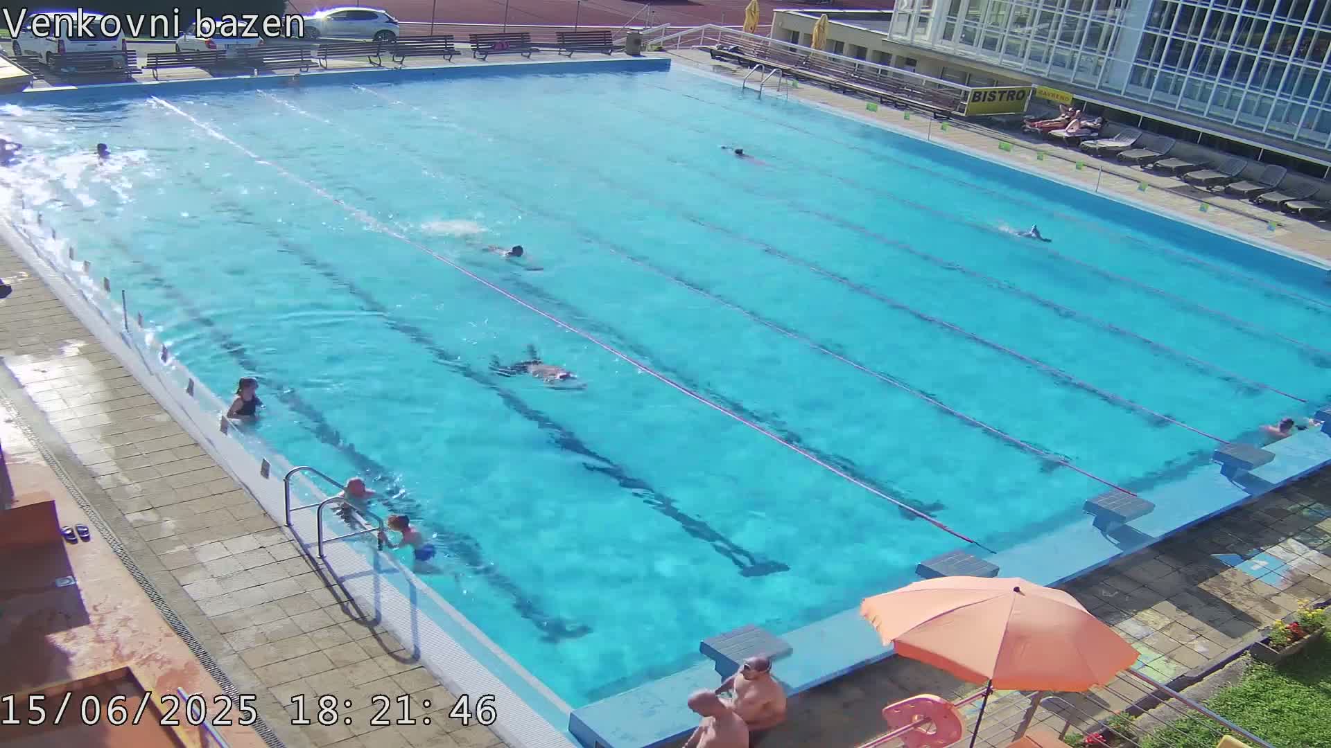 An outdoor swimming pool with several people swimming and lounging on a sunny day.