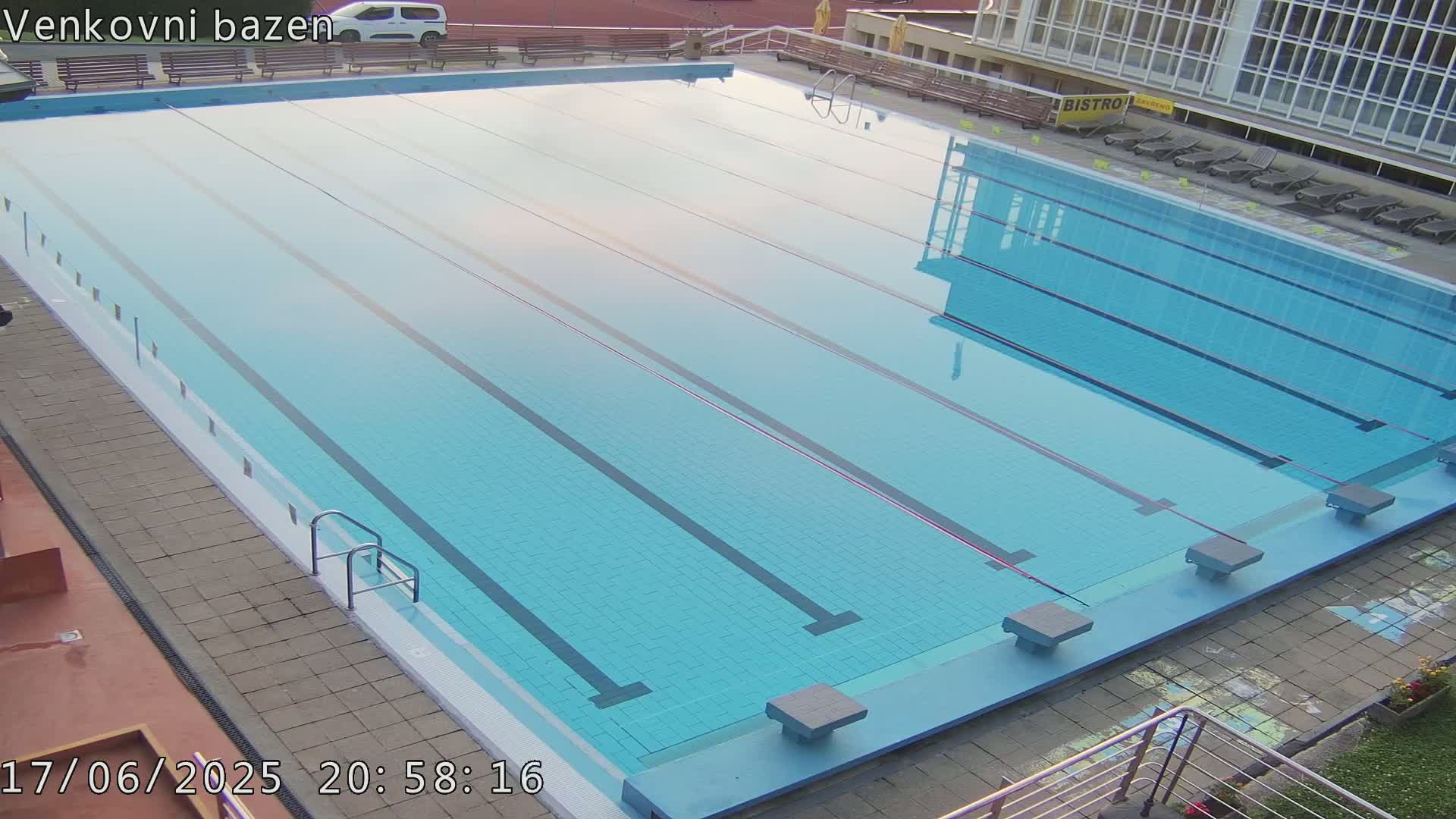 An outdoor swimming pool with multiple lanes is mostly empty under a clear evening sky.