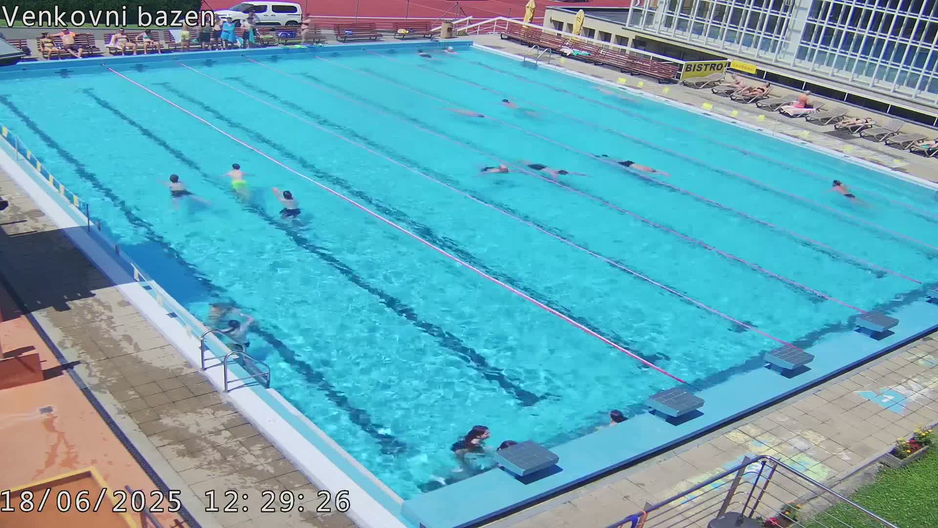 A large outdoor swimming pool with multiple people swimming in it on a sunny day.