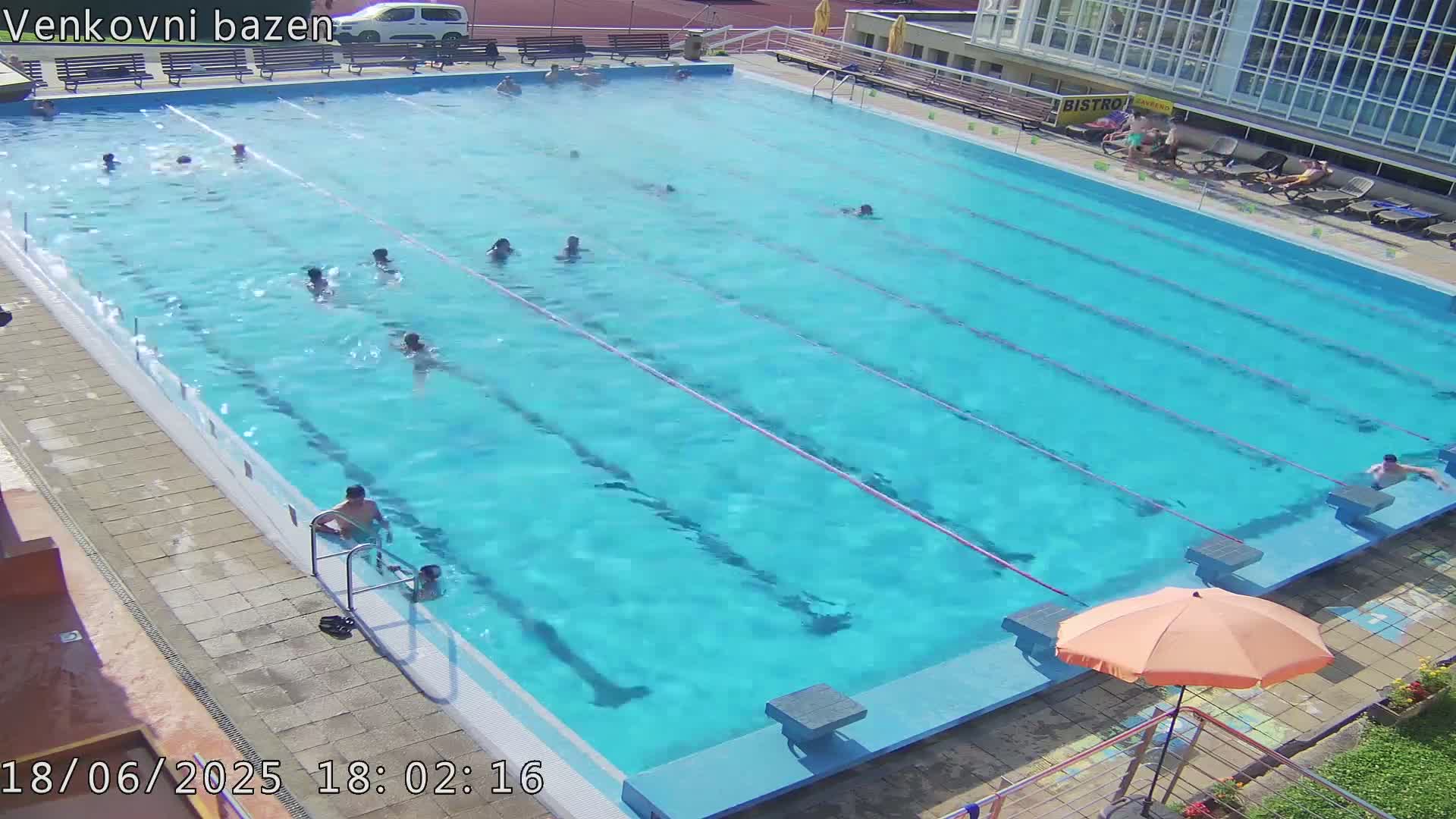A large outdoor swimming pool with numerous people swimming in it on a sunny day.