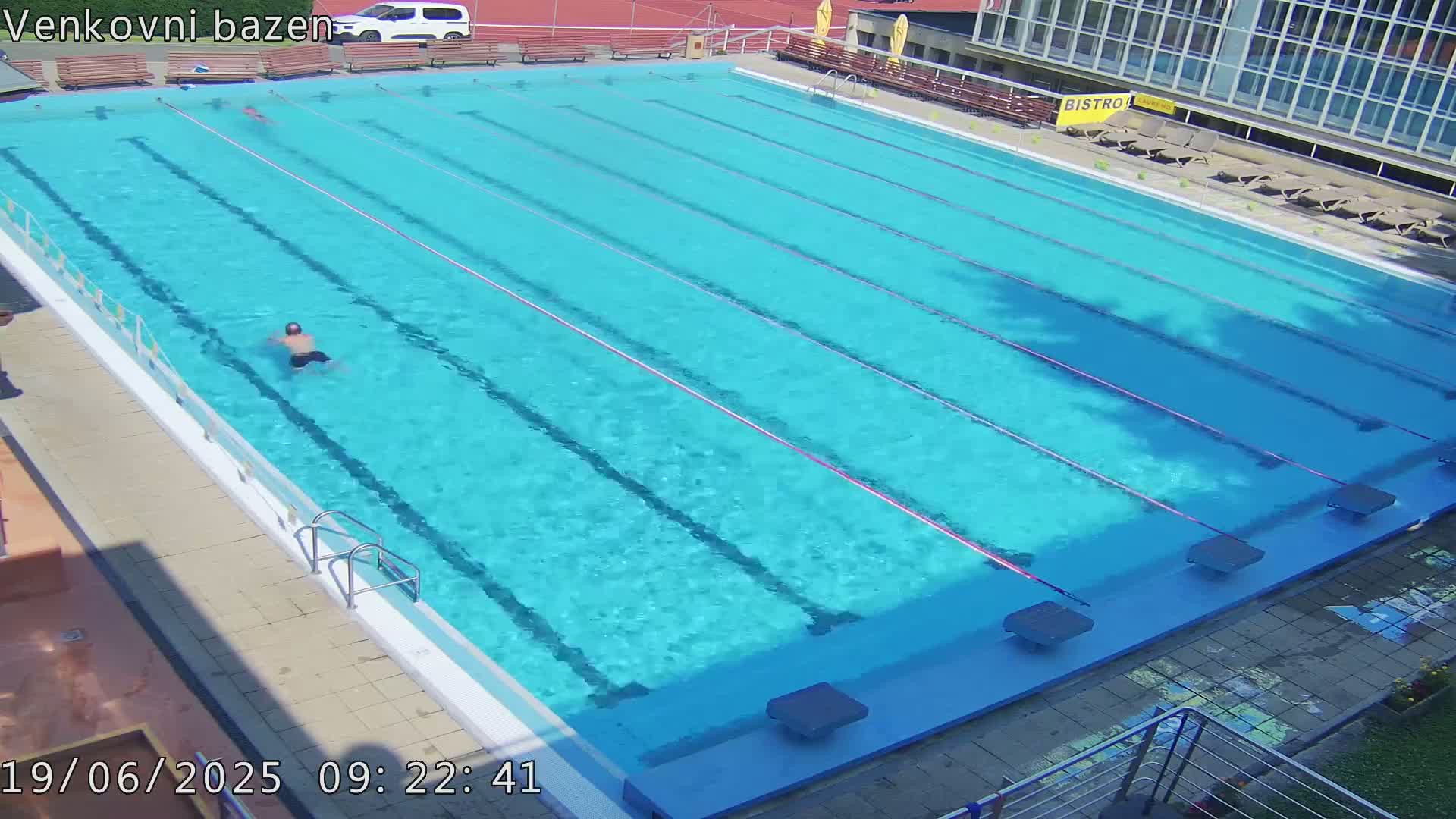 A person swims laps in a large outdoor swimming pool on a sunny day.