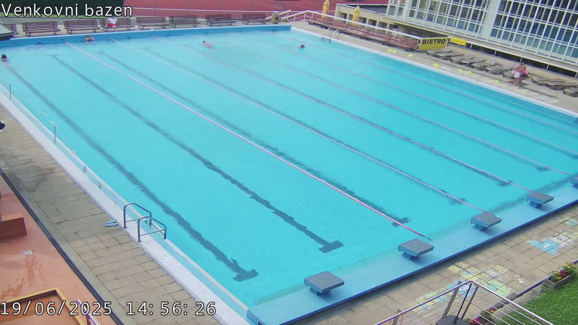 A large outdoor swimming pool with several people swimming in it, under a clear sky.