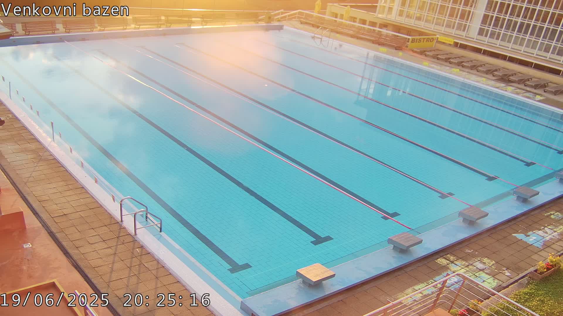 An outdoor swimming pool with multiple lanes is illuminated by the setting sun.