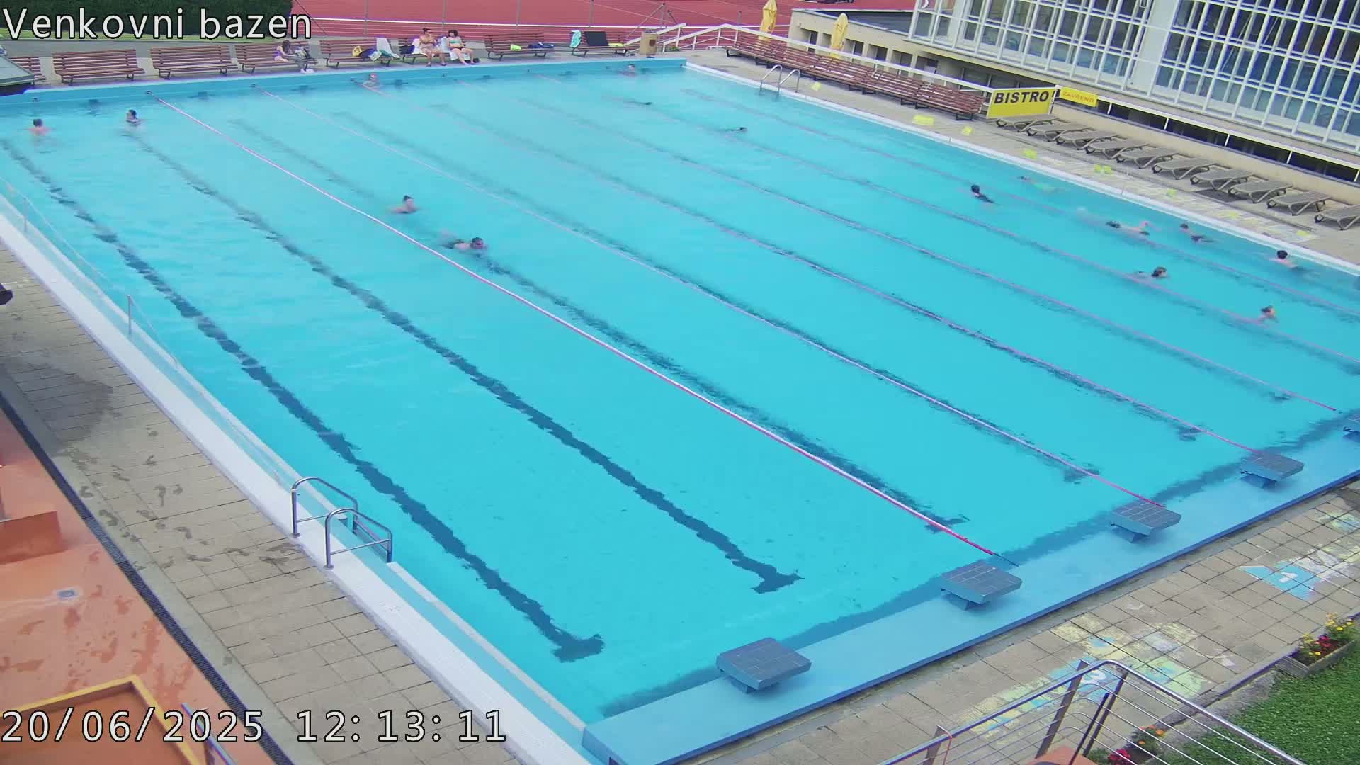 A large outdoor swimming pool with several people swimming in its clear, blue water.
