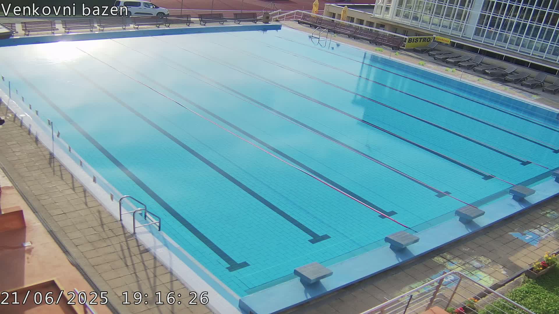 An empty, light-blue swimming pool with lane dividers is outdoors in sunny weather.