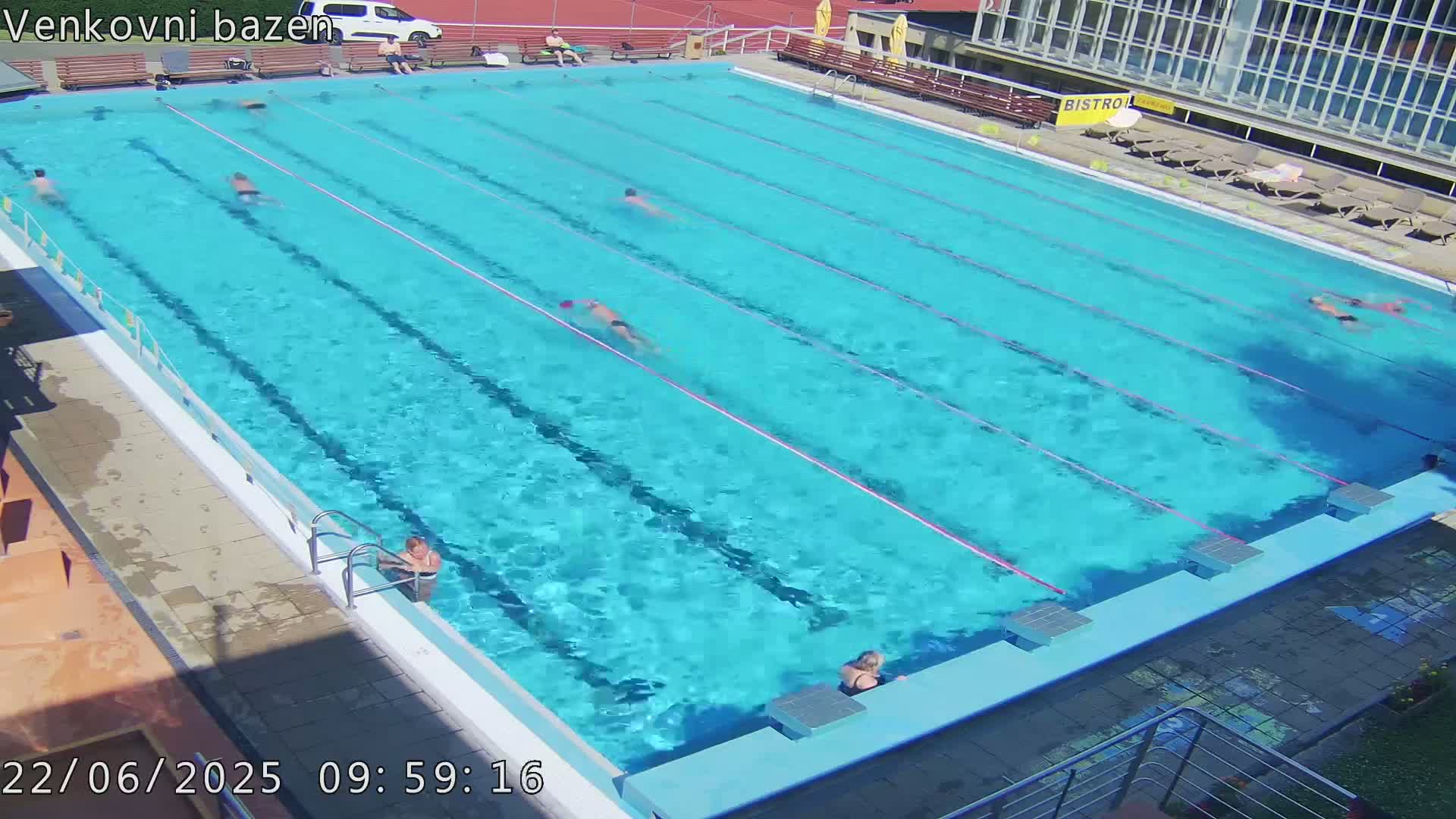A sunny day at an outdoor swimming pool with several people swimming and lounging.