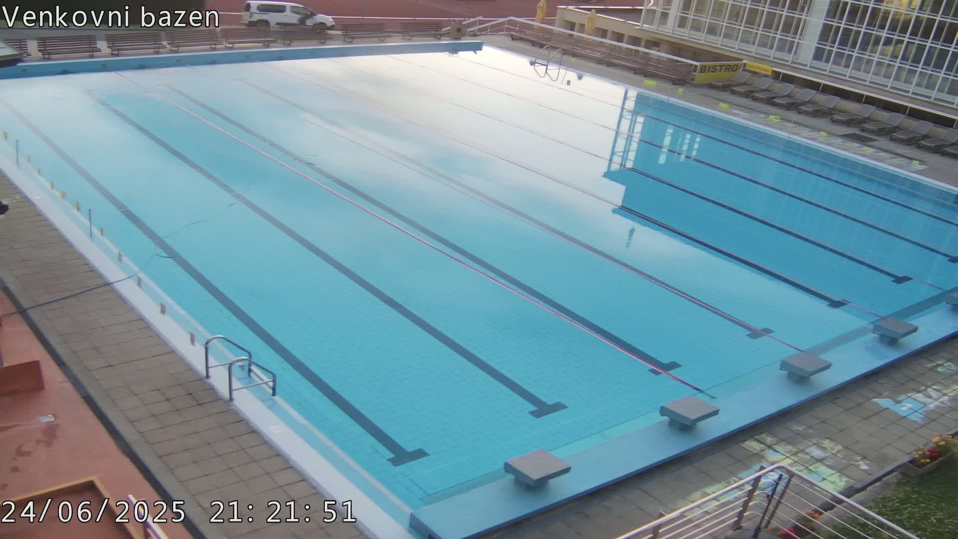 An empty, light-blue outdoor swimming pool with multiple lanes is seen at night.