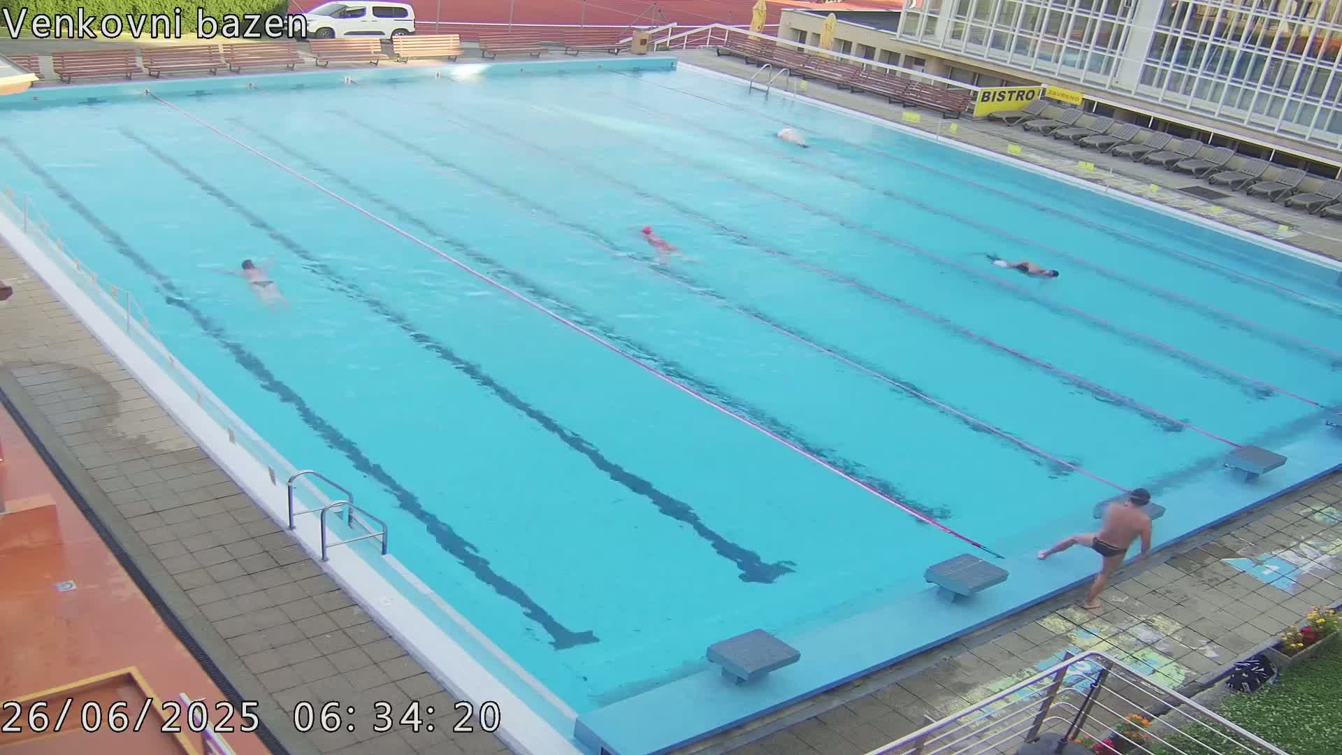 An empty, light-blue outdoor swimming pool with multiple lanes is seen at night.