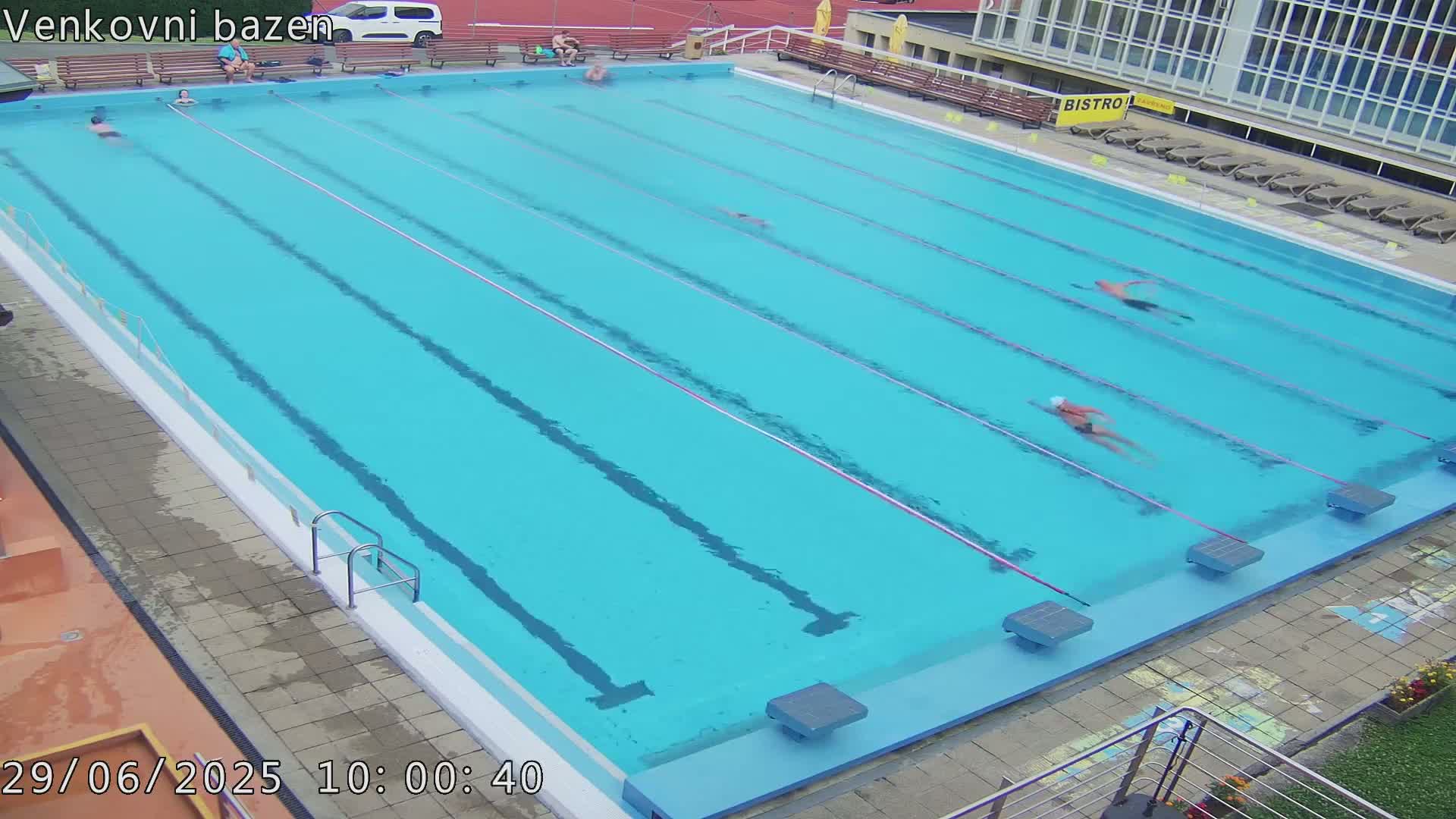 An outdoor swimming pool with several people swimming laps in clear blue water.