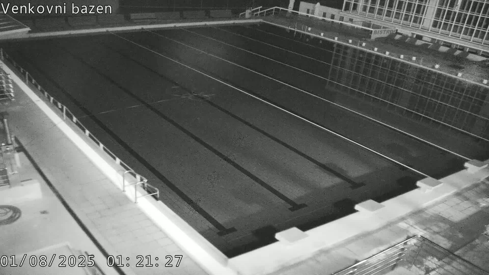 An empty, dark swimming pool with lane dividers is visible at night.