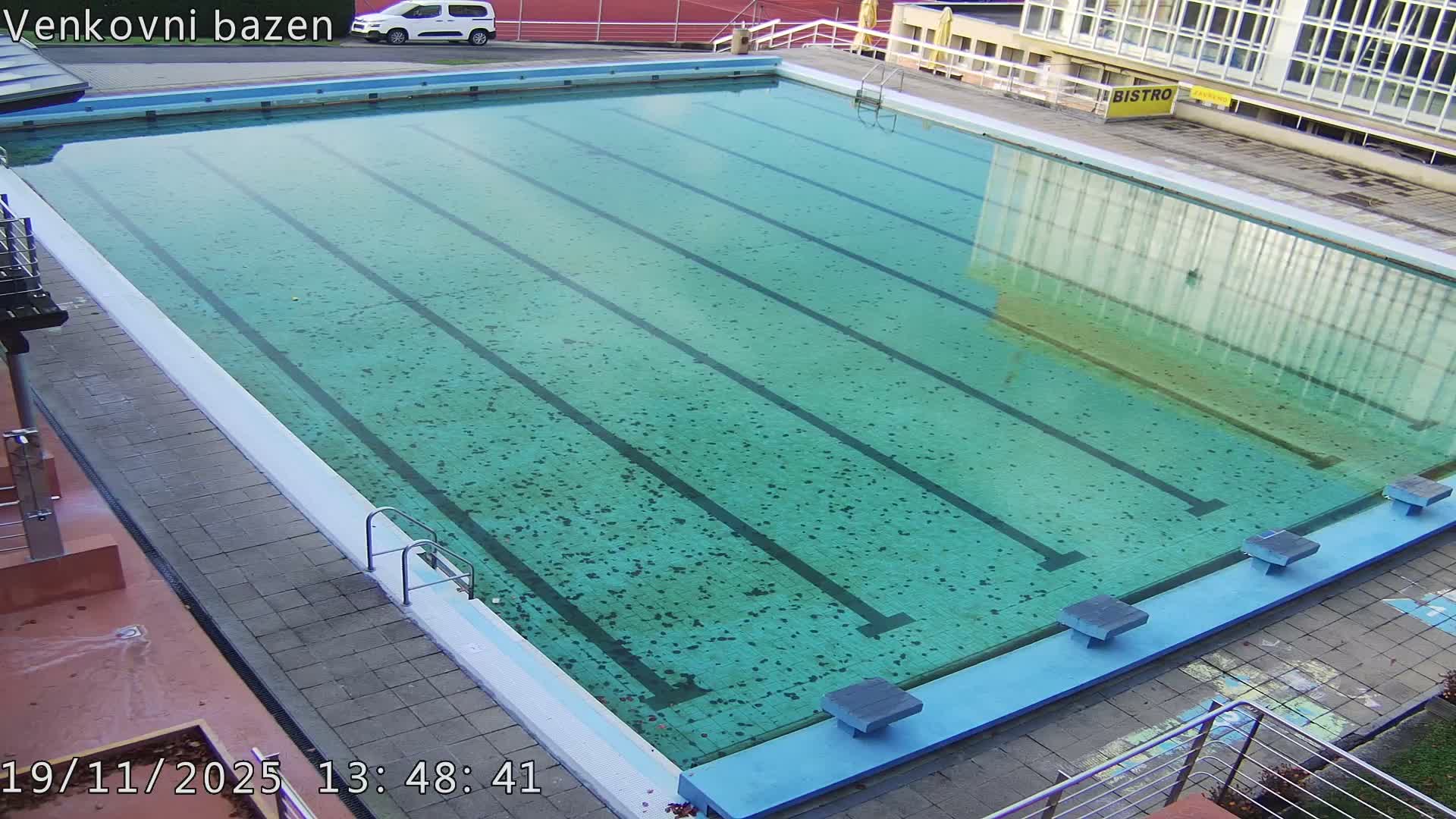 An outdoor swimming pool with several people swimming laps in a sunny day.