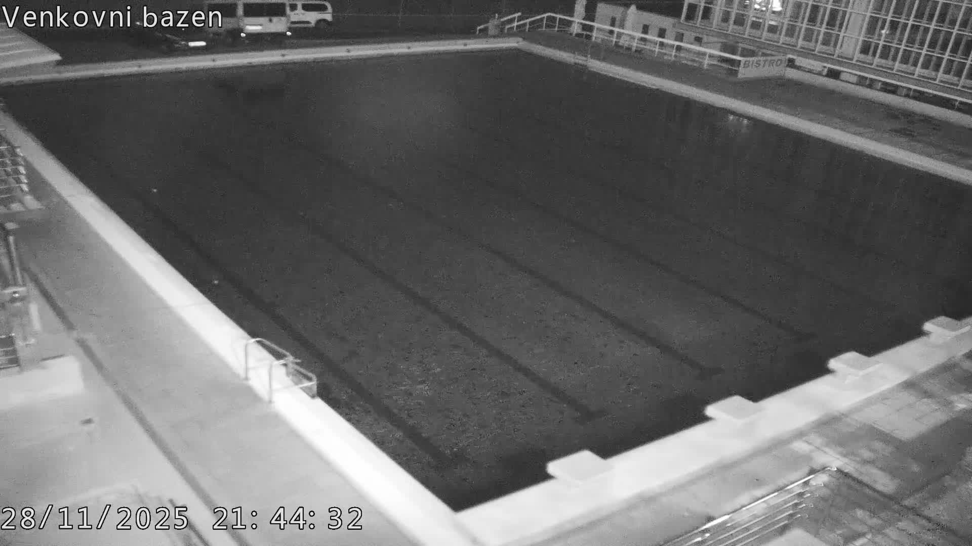 A grainy, black and white night vision view captures an empty outdoor swimming pool under clear, calm night conditions.