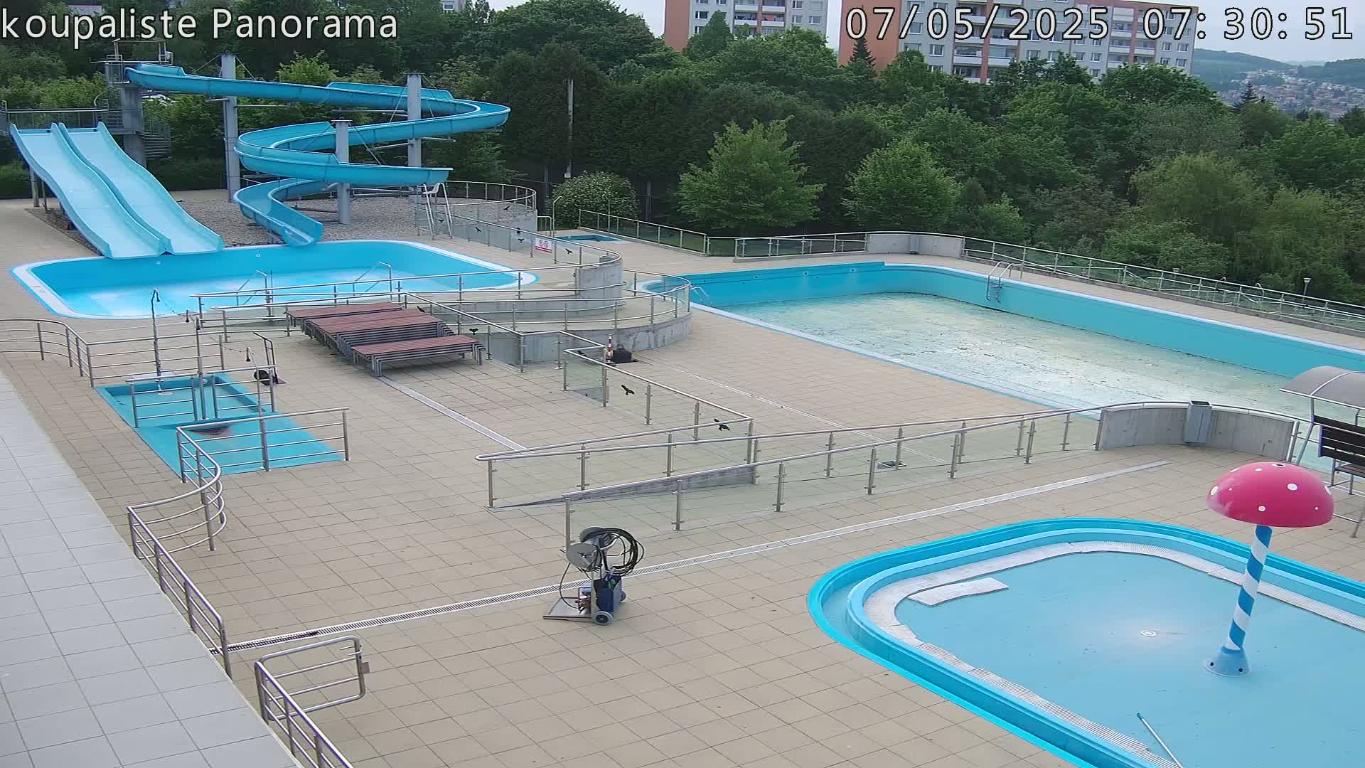 An outdoor pool complex with several pools, slides, and a mushroom-shaped water feature, under a mostly clear sky.