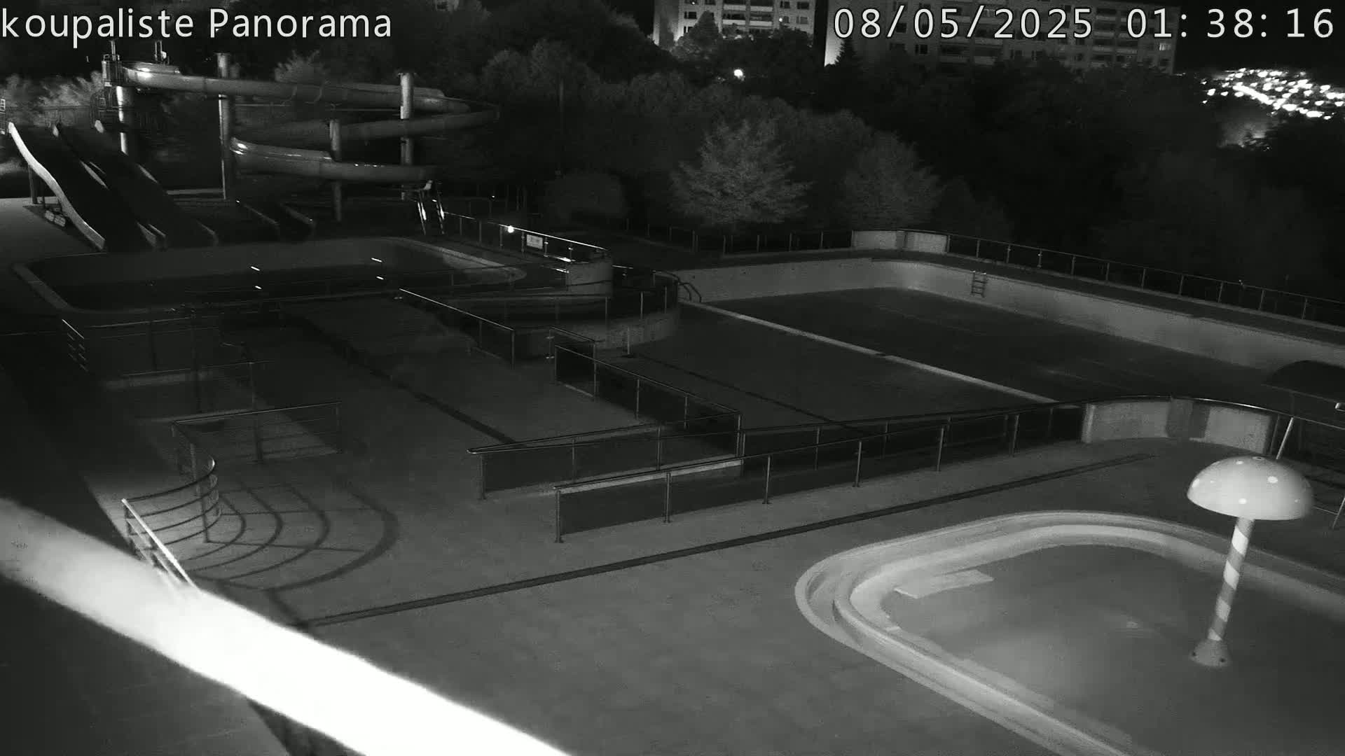 An outdoor nighttime view of an empty swimming complex with water slides, several pools, and handrails.