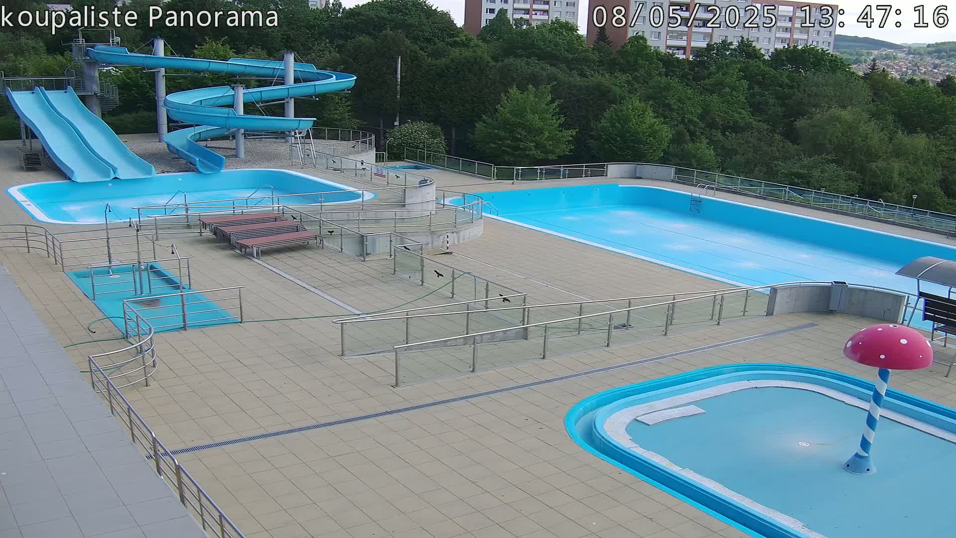An outdoor pool complex with multiple pools, slides, and ramps, on a sunny day.