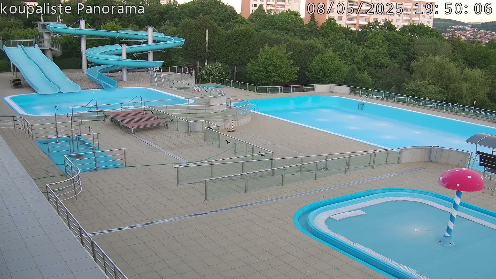 An outdoor pool complex with multiple pools, slides, and a small mushroom-shaped water feature, under an overcast sky.
