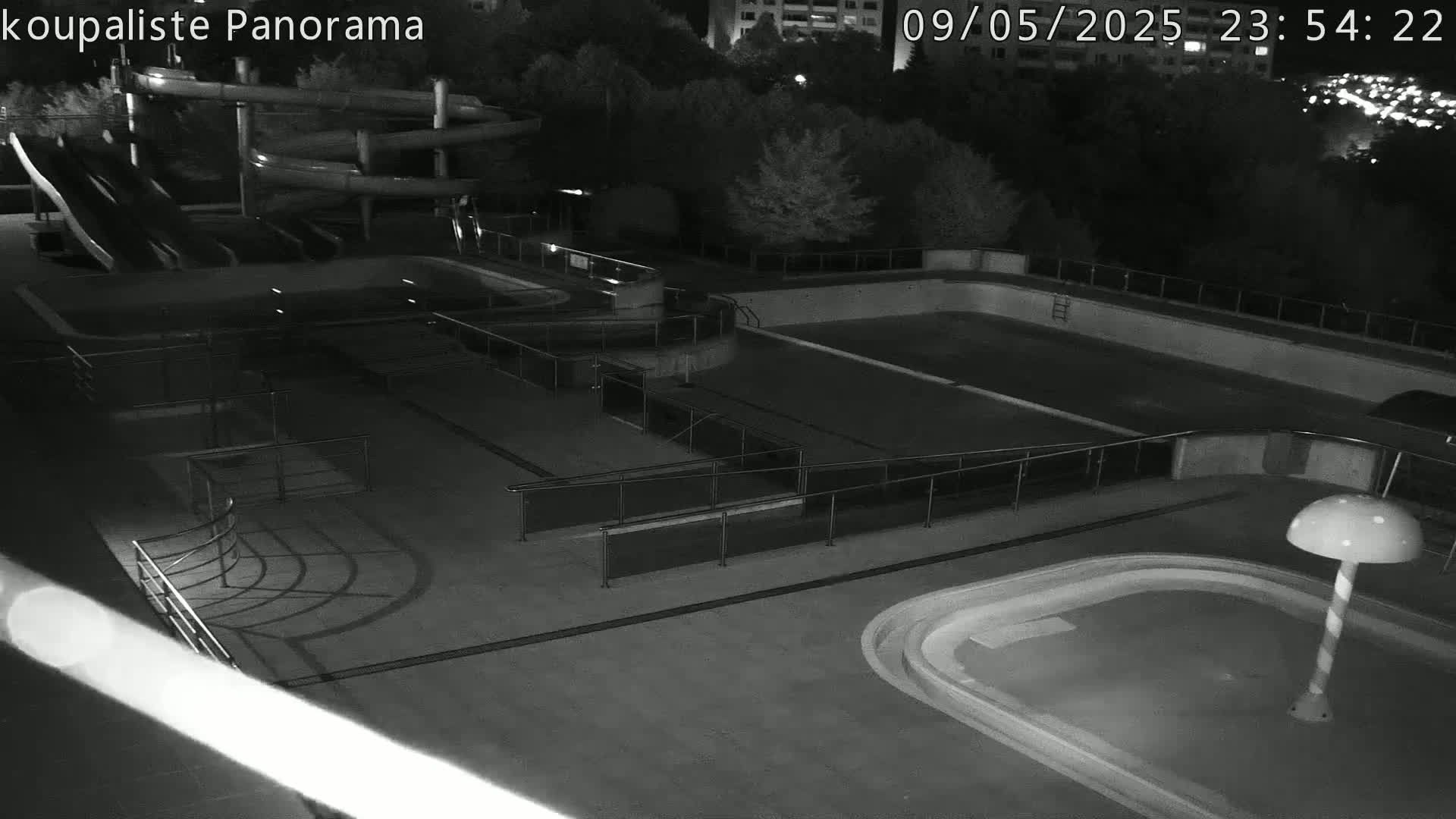 An empty outdoor swimming pool complex with water slides is shown at night.