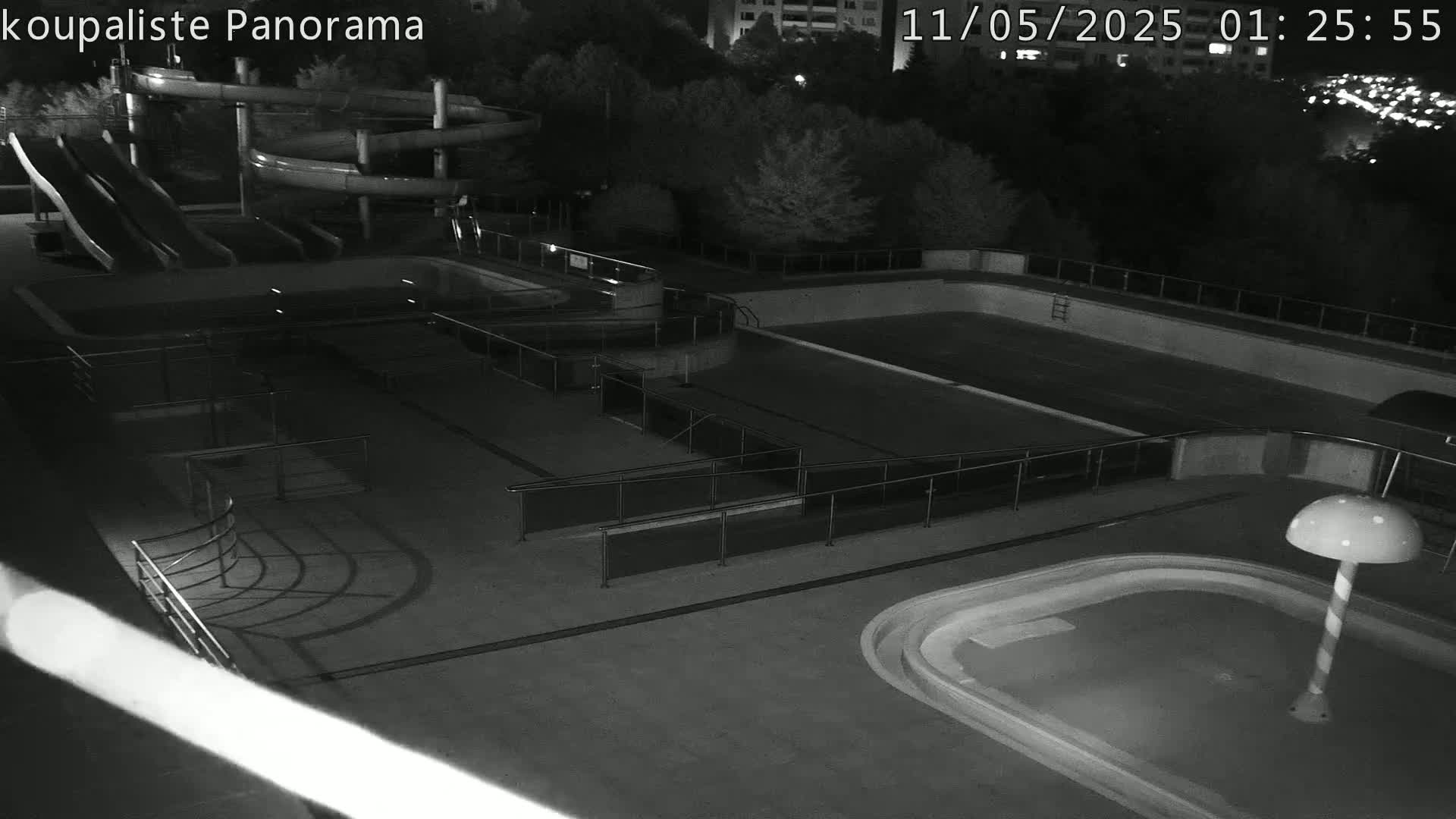 An empty outdoor swimming pool complex with water slides is seen at night under dark conditions.